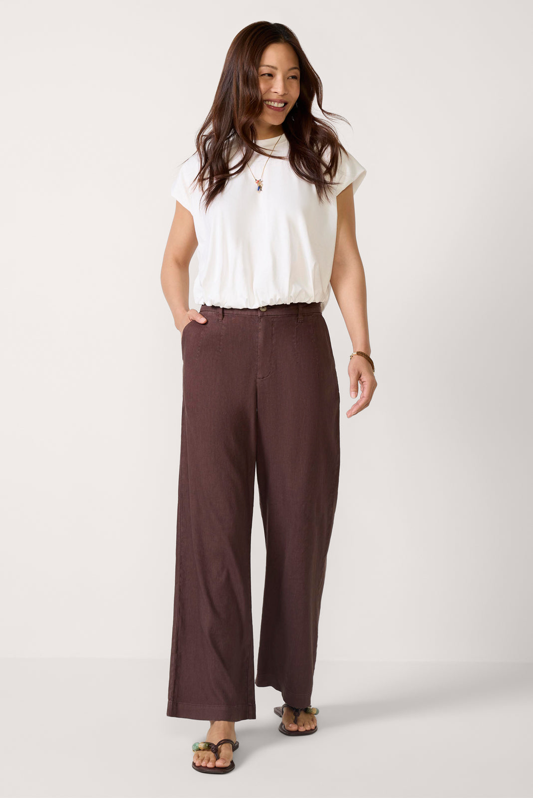 Woman wearing white top and chocolate brown wide-leg linen pants with sandals