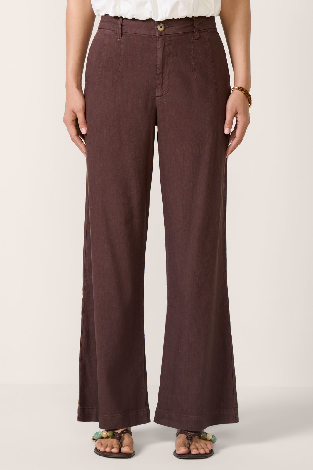 Woman wearing chocolate brown wide-leg linen pants with white top and sandals