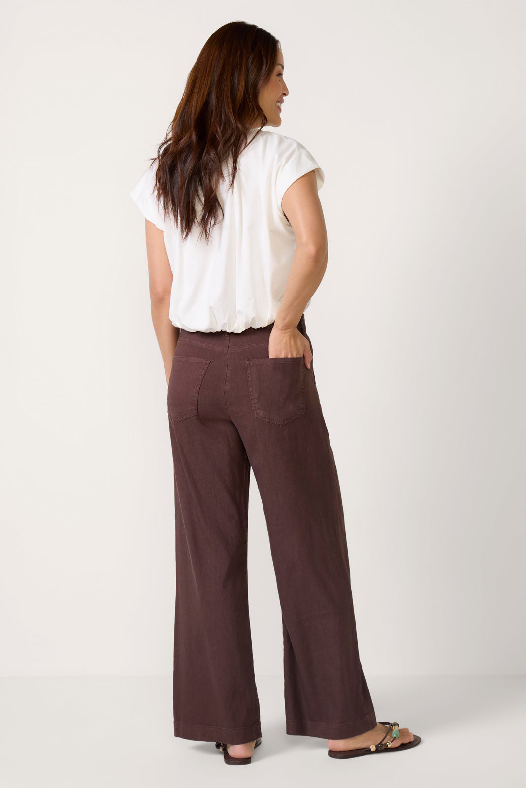 Woman wearing chocolate brown wide-leg linen pants with white top, back view