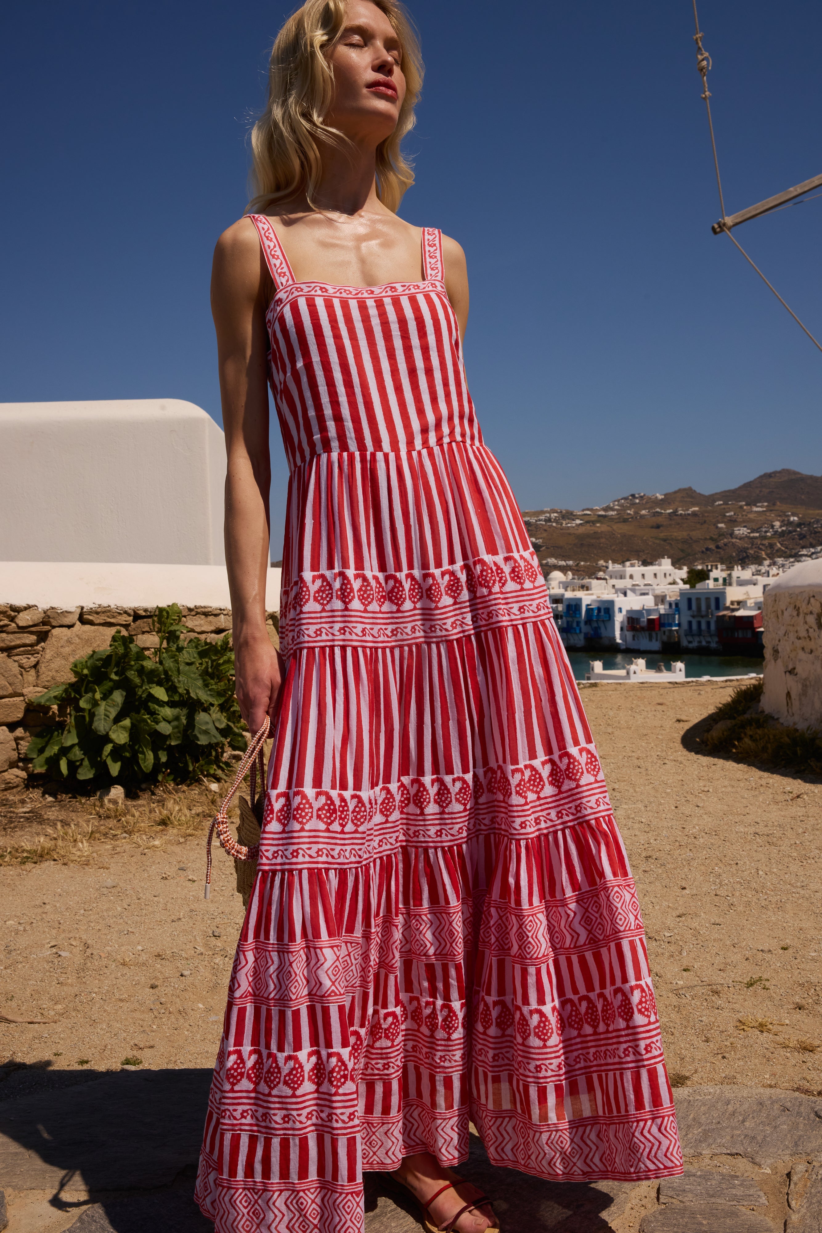 Woman wearing red and white striped maxi dress with decorative trim in Greek island setting