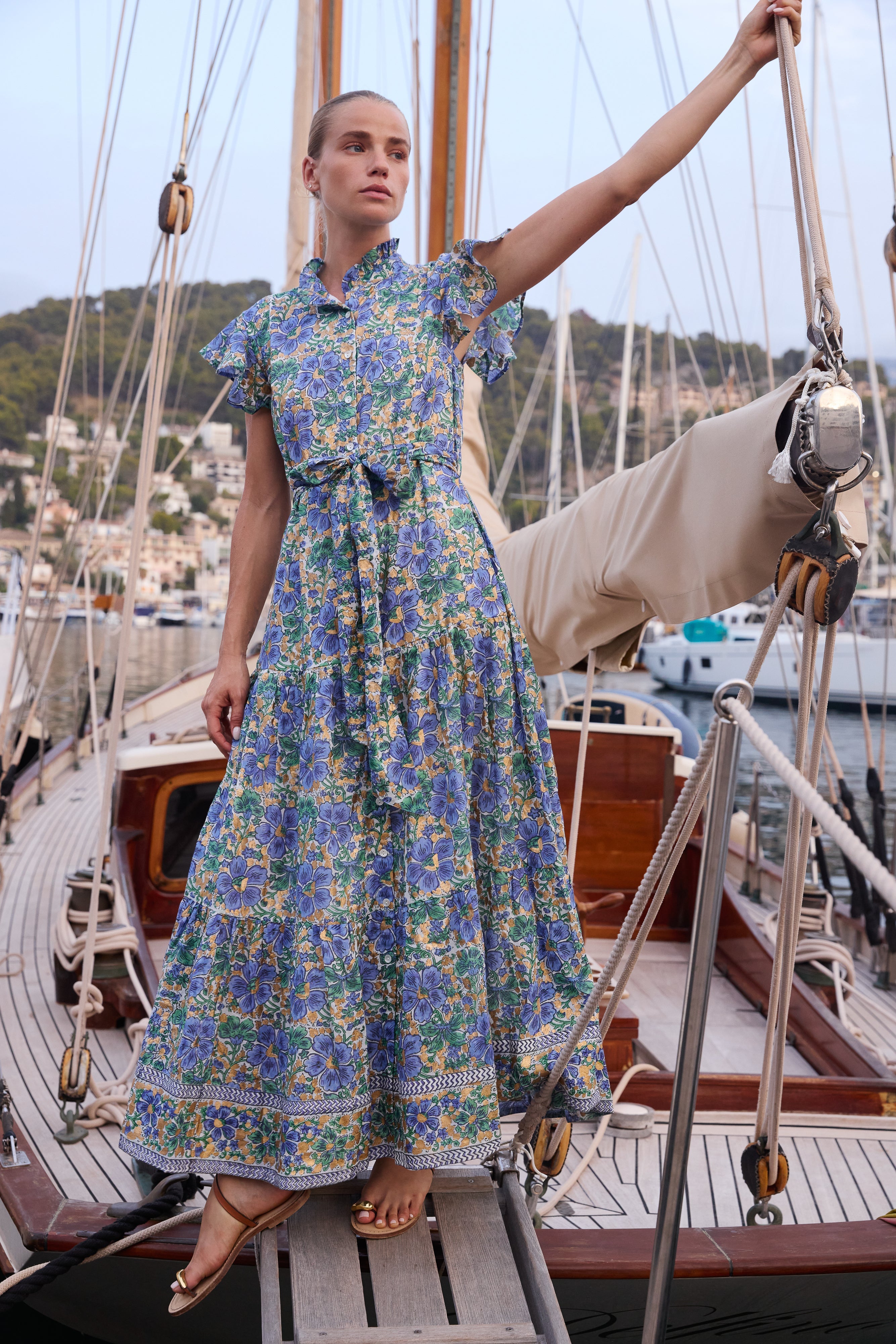 Woman wearing blue floral maxi dress with ruffle collar on sailboat deck