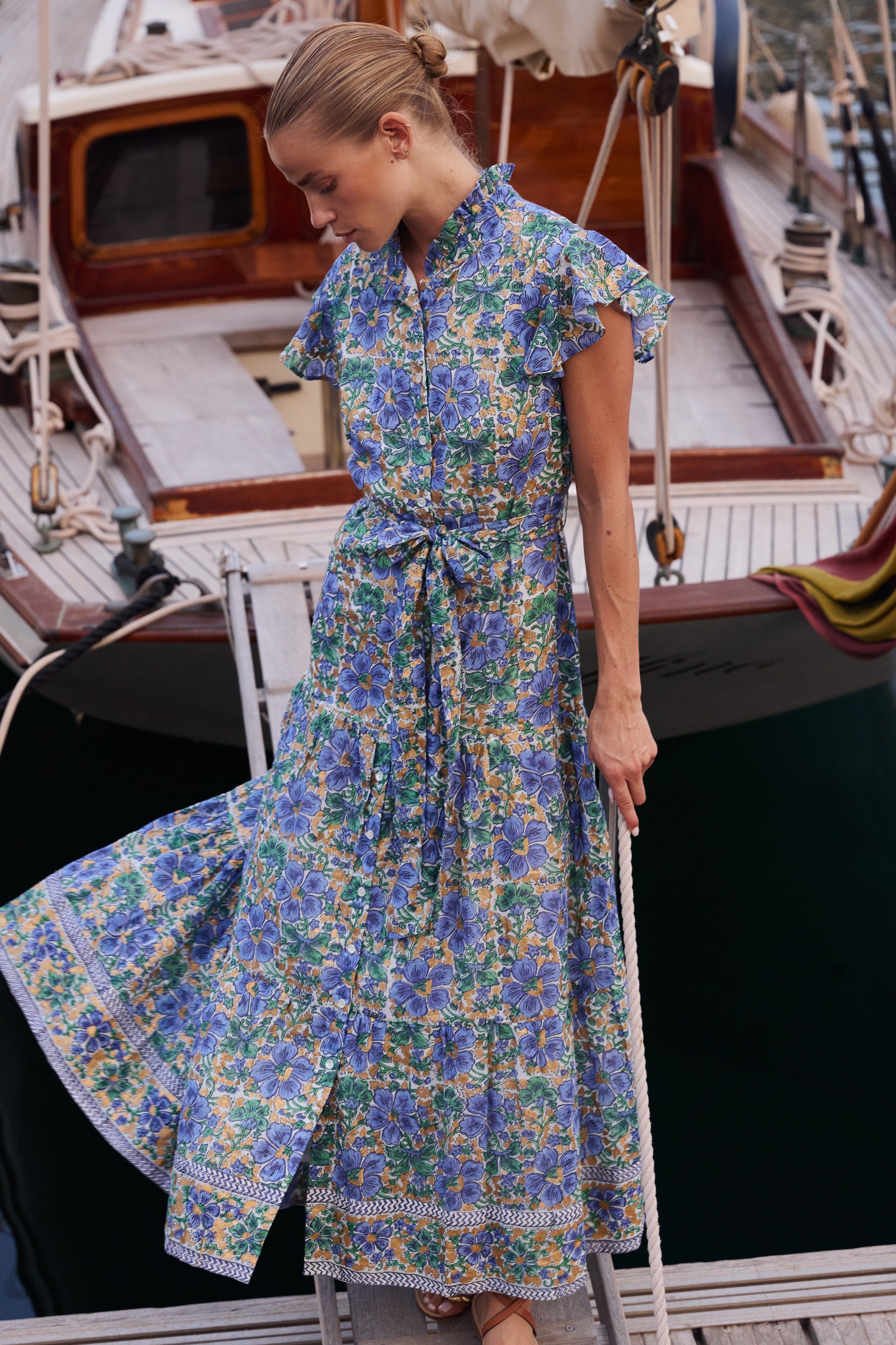 Woman wearing blue floral maxi dress with ruffle collar on yacht deck