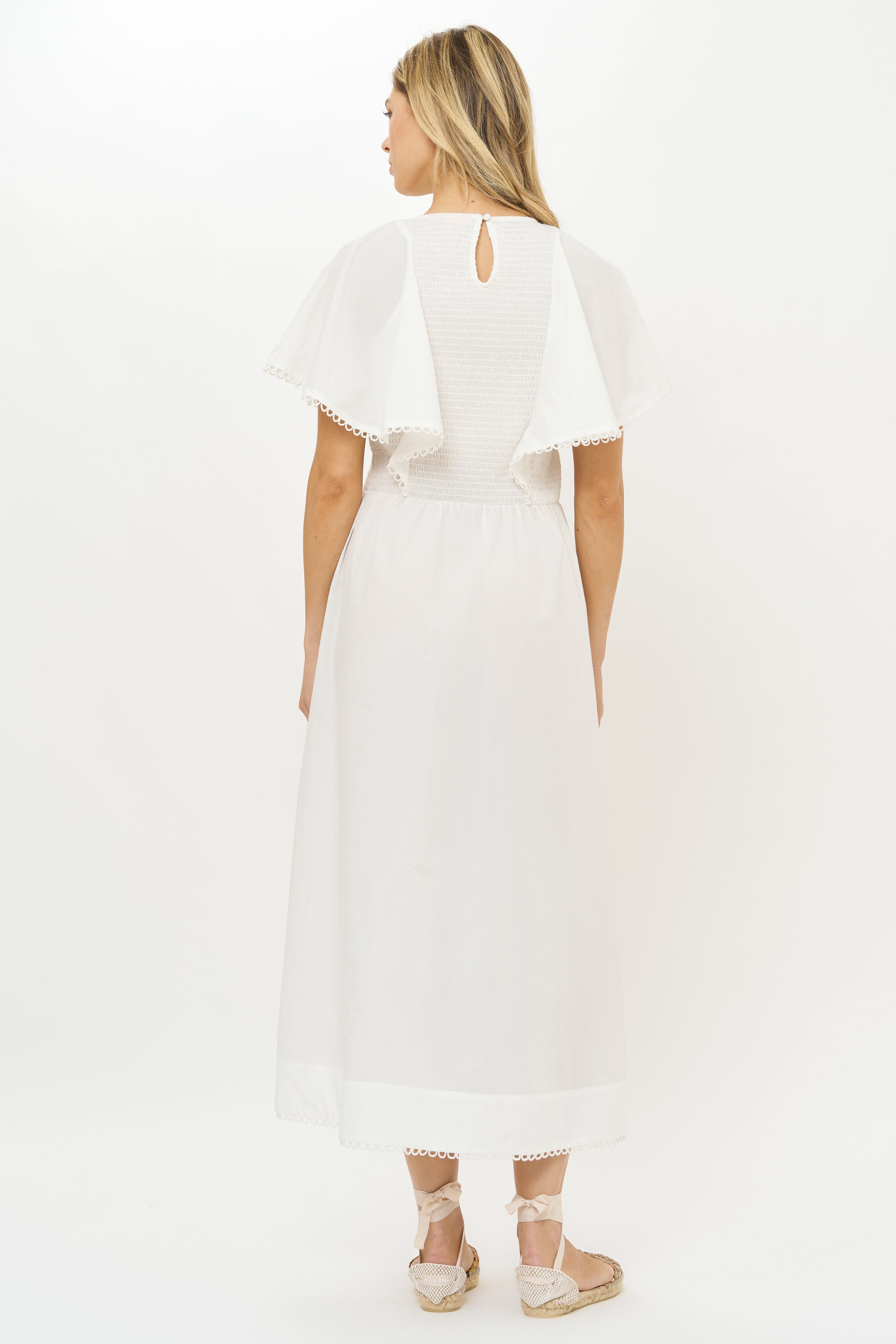 Back view of blonde woman wearing white eyelet midi dress with flutter sleeves and lace trim