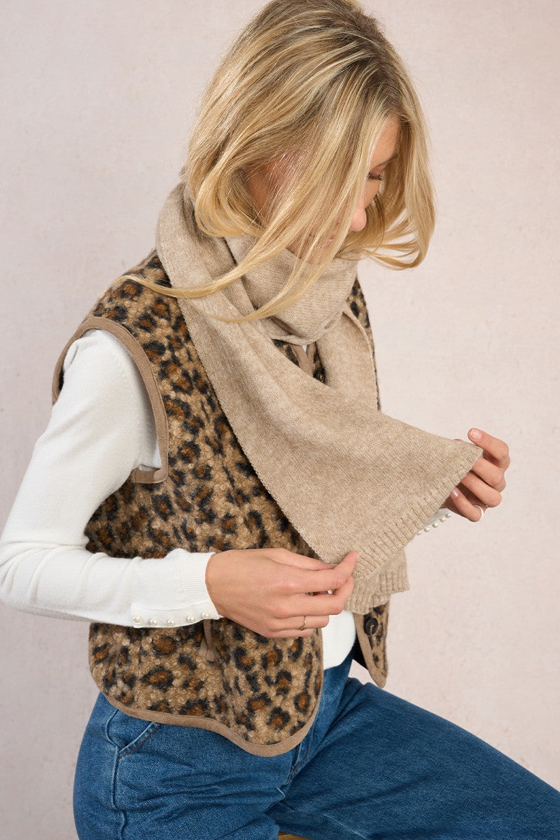 Woman wearing beige bow scarf with leopard print vest and white shirt