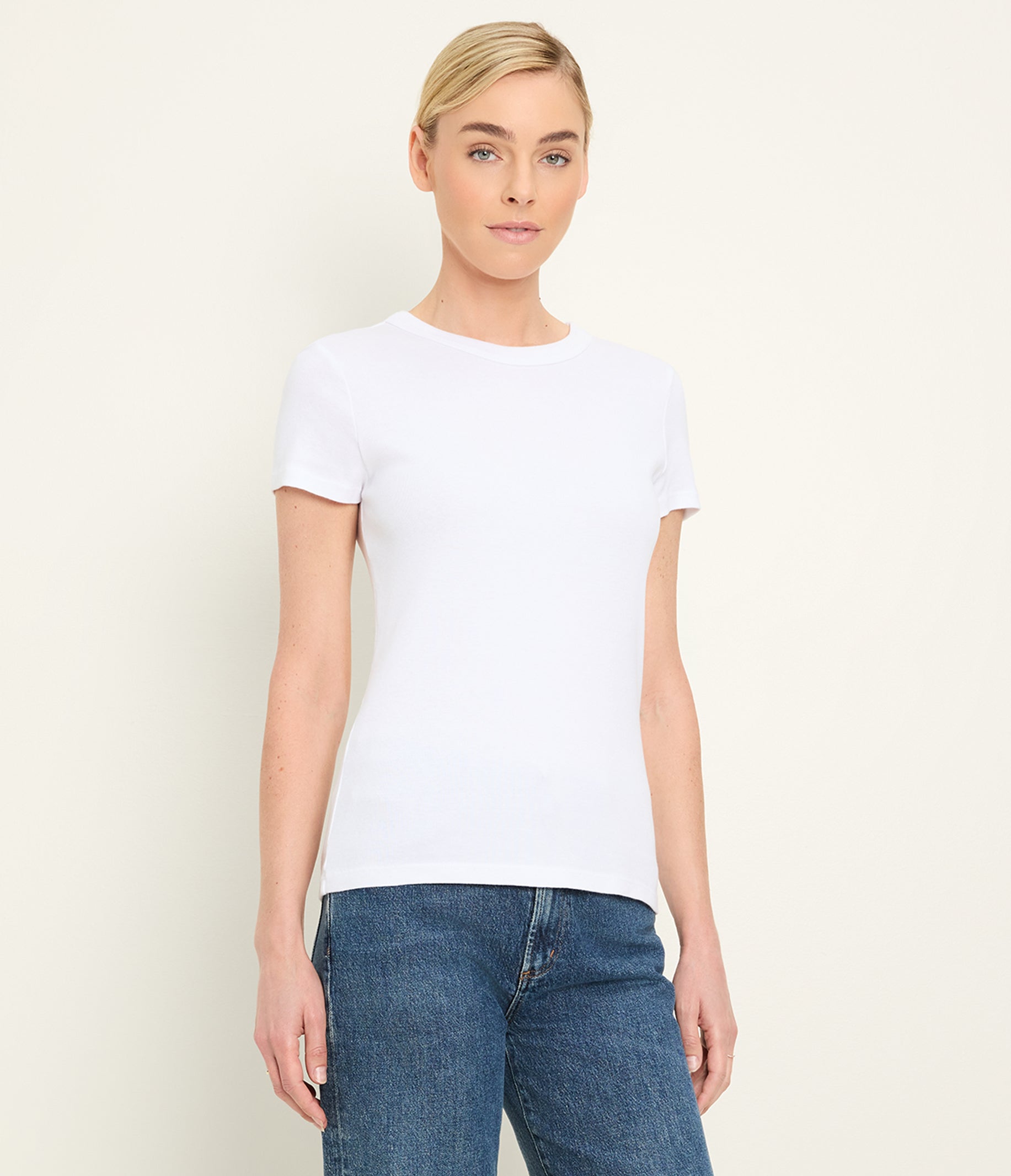 Woman wearing white crew neck t-shirt with blue jeans against neutral background