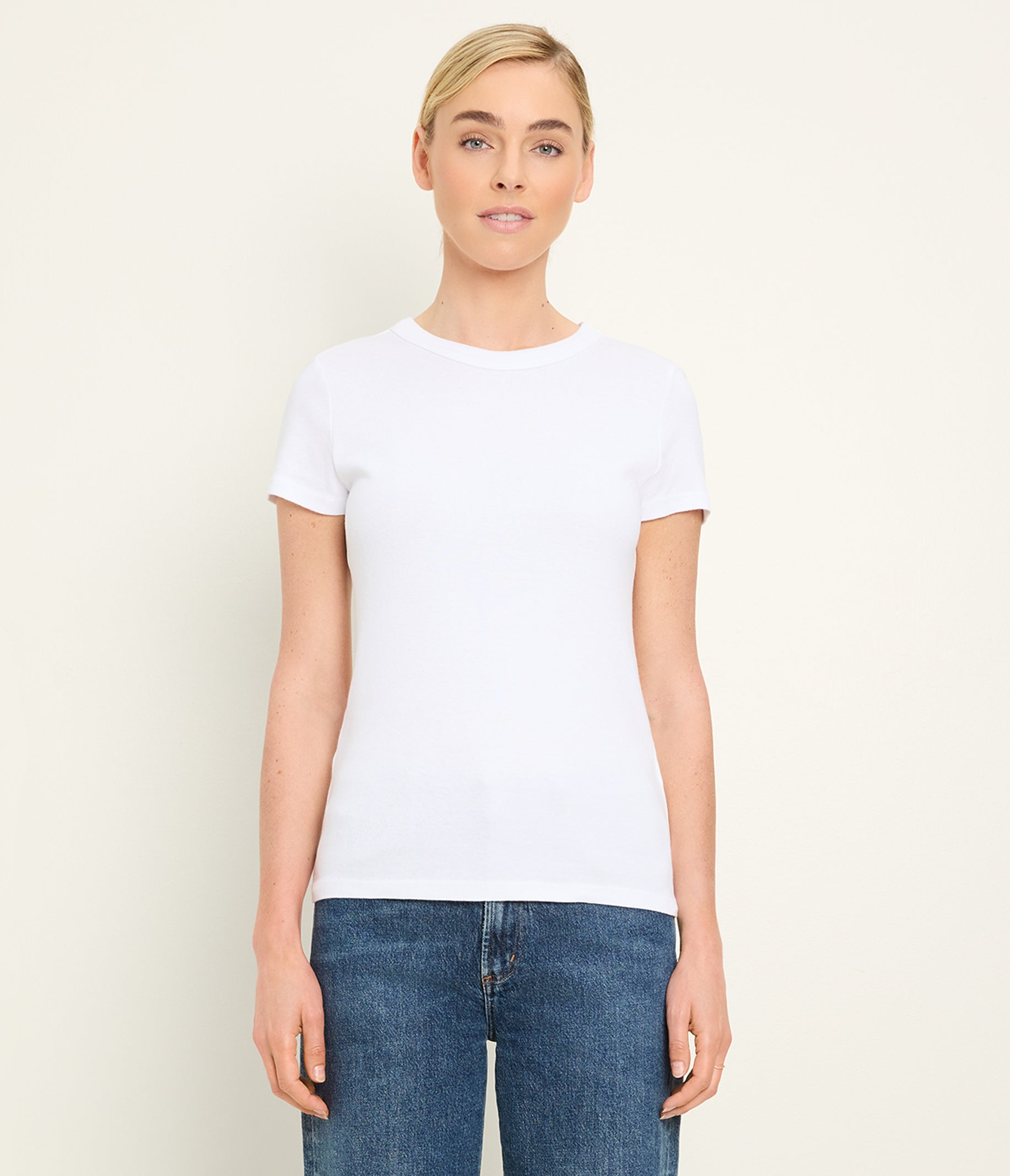Woman wearing white short-sleeve crew neck t-shirt with blue jeans against neutral background