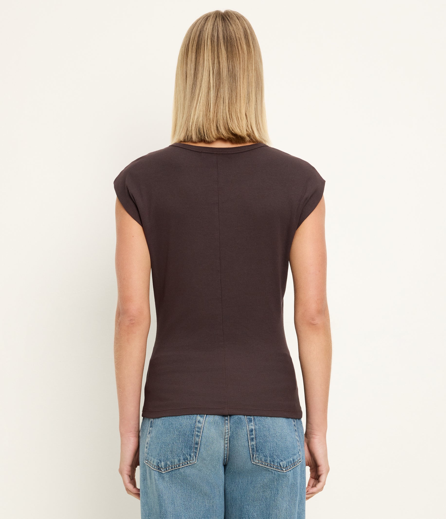 Back view of woman wearing brown sleeveless crew neck top with blue jeans