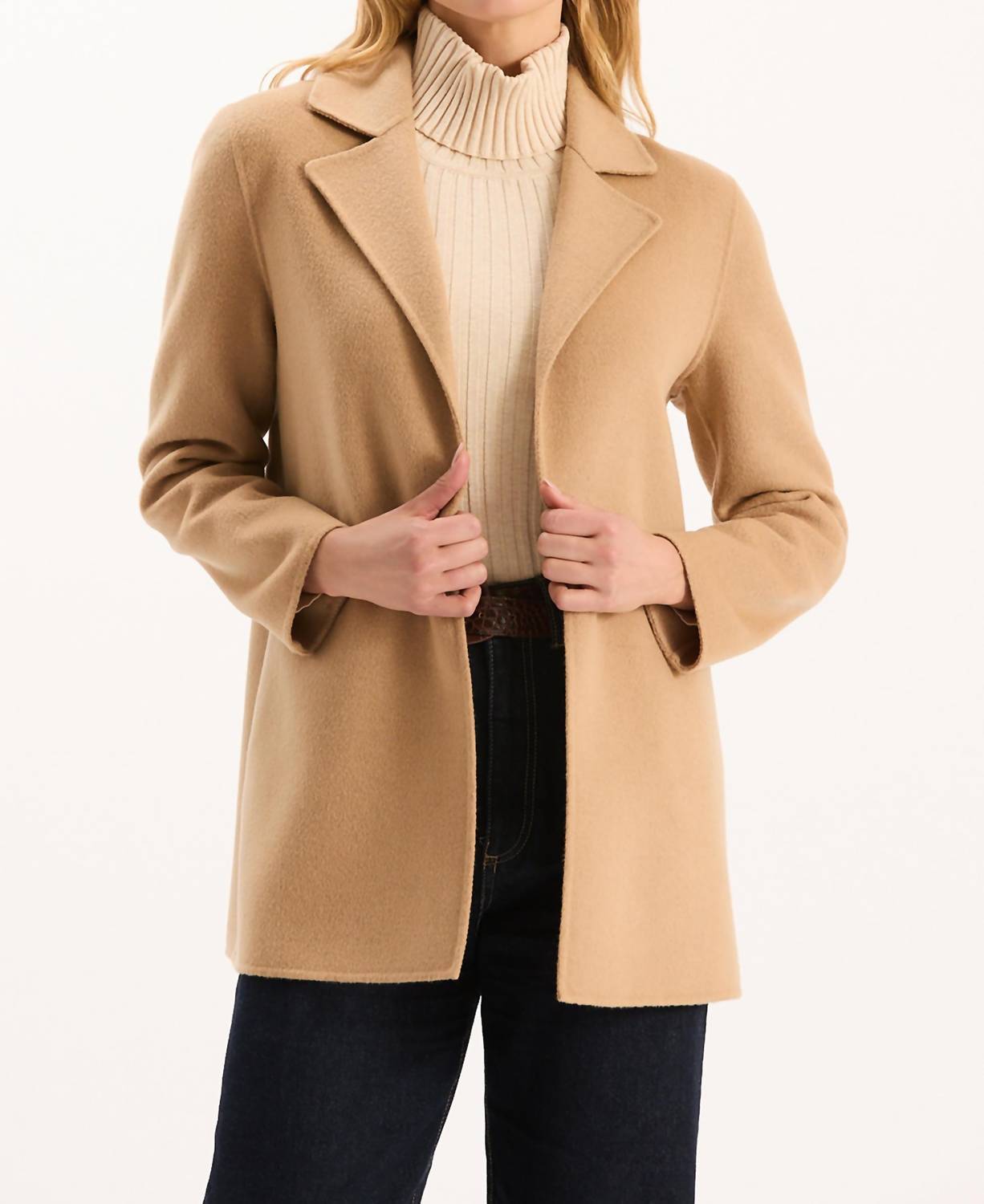 Woman wearing camel-colored wool car coat over cream turtleneck sweater and dark jeans