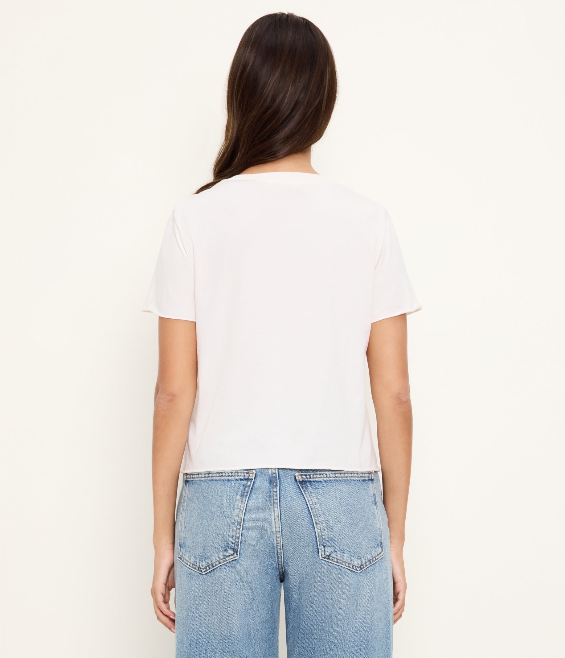 Back view of woman wearing white cropped t-shirt with rolled sleeves and light blue jeans