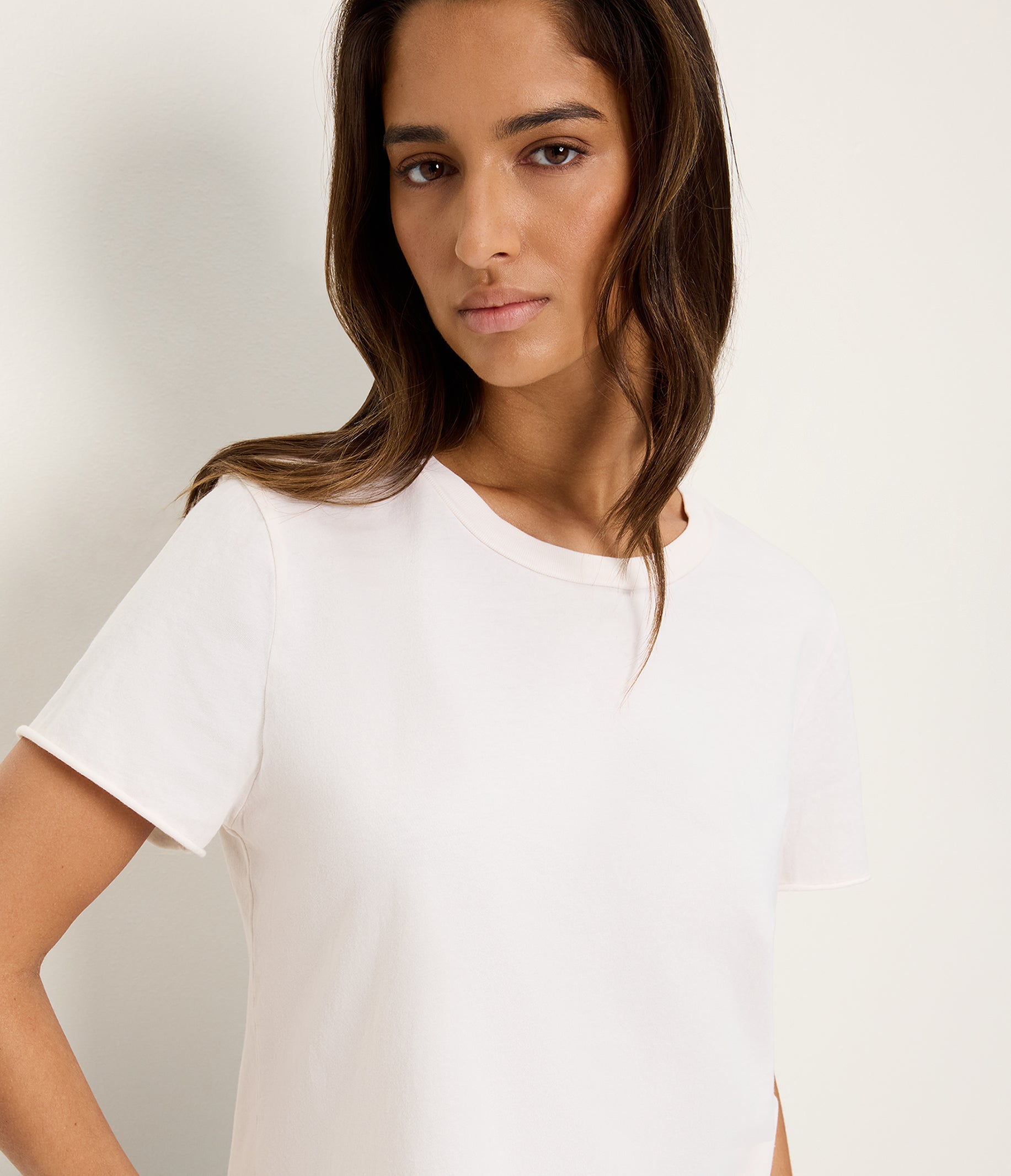 Woman wearing white short-sleeve crop tee with rolled hem against neutral background