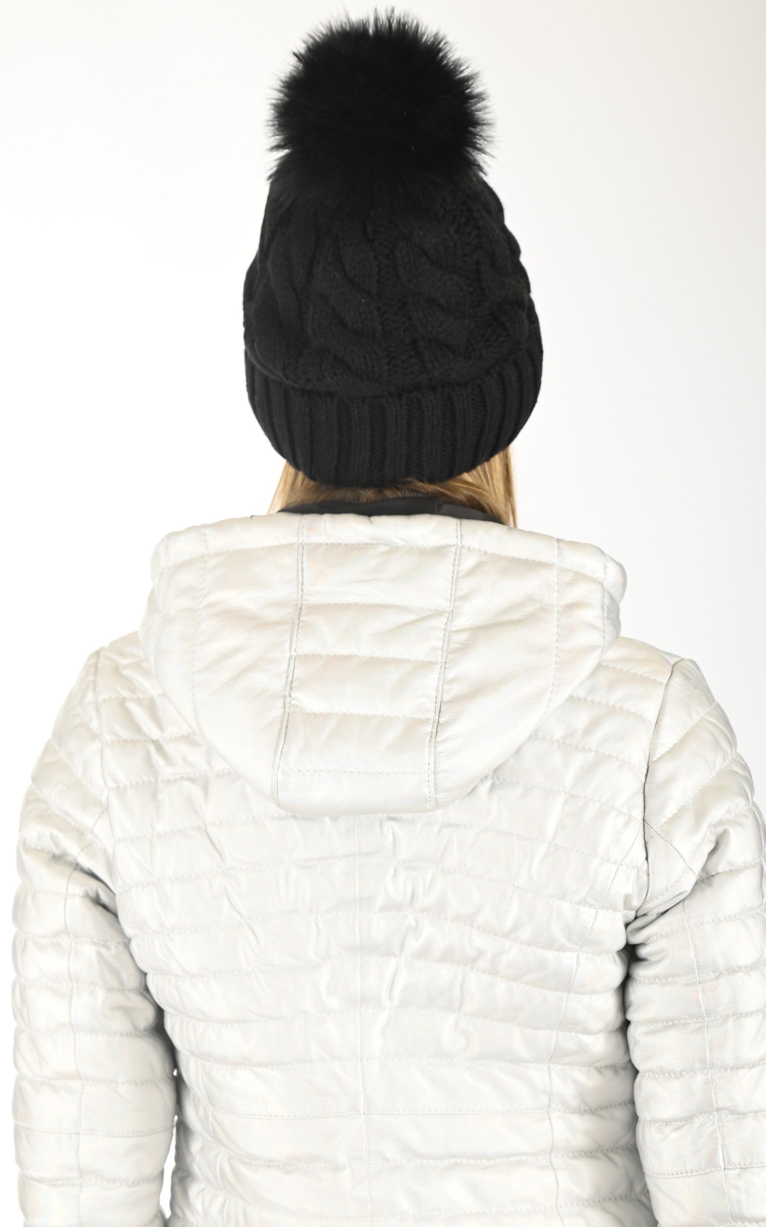 Black cable-knit beanie with fur pom-pom worn with white quilted jacket, back view