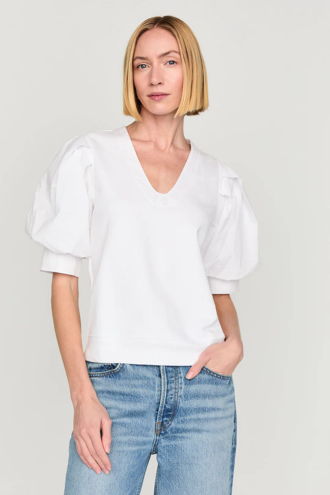 Woman wearing white v-neck popover top with puff sleeves and blue jeans