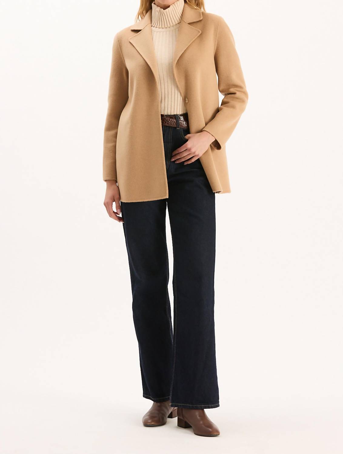 Woman wearing camel-colored car coat over cream turtleneck sweater and dark jeans
