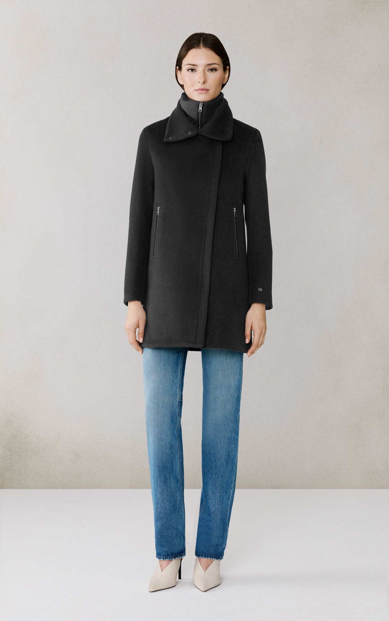 Woman wearing black wool coat with high collar and zipper details over blue jeans
