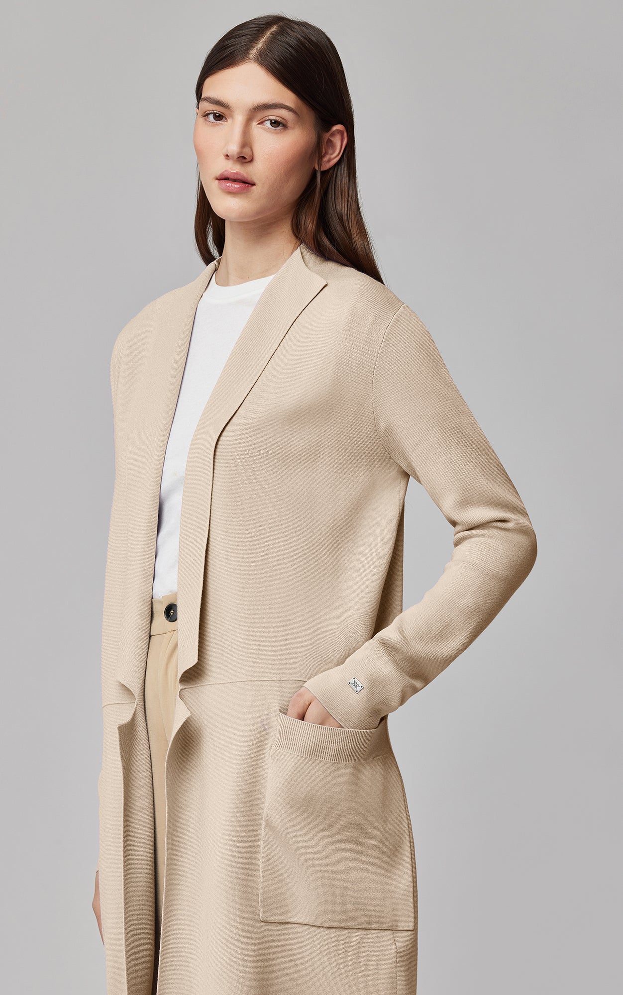 Woman wearing beige long cardigan over white top in studio setting