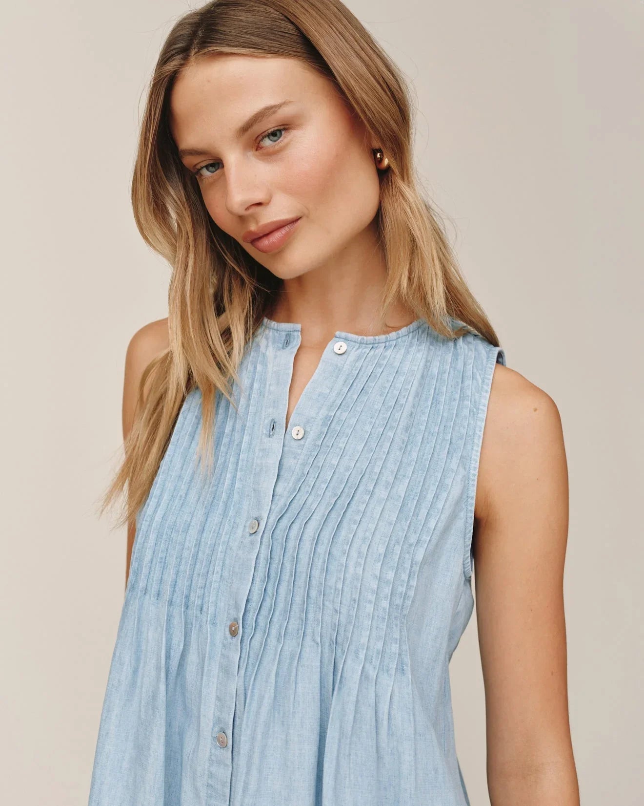 Woman wearing light blue sleeveless pintuck dress with button front detail