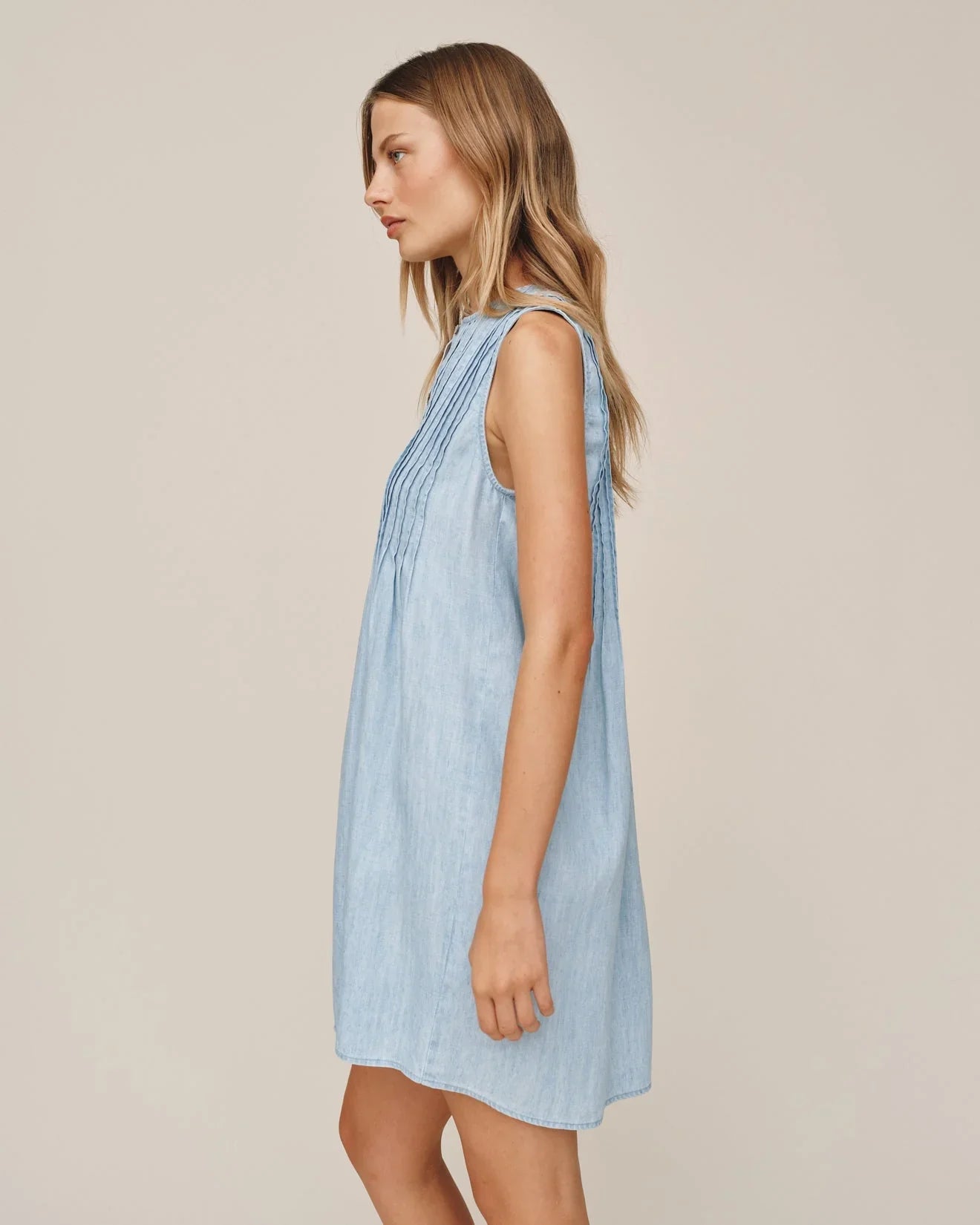 Woman wearing light blue sleeveless pintuck dress in sun bleached denim wash