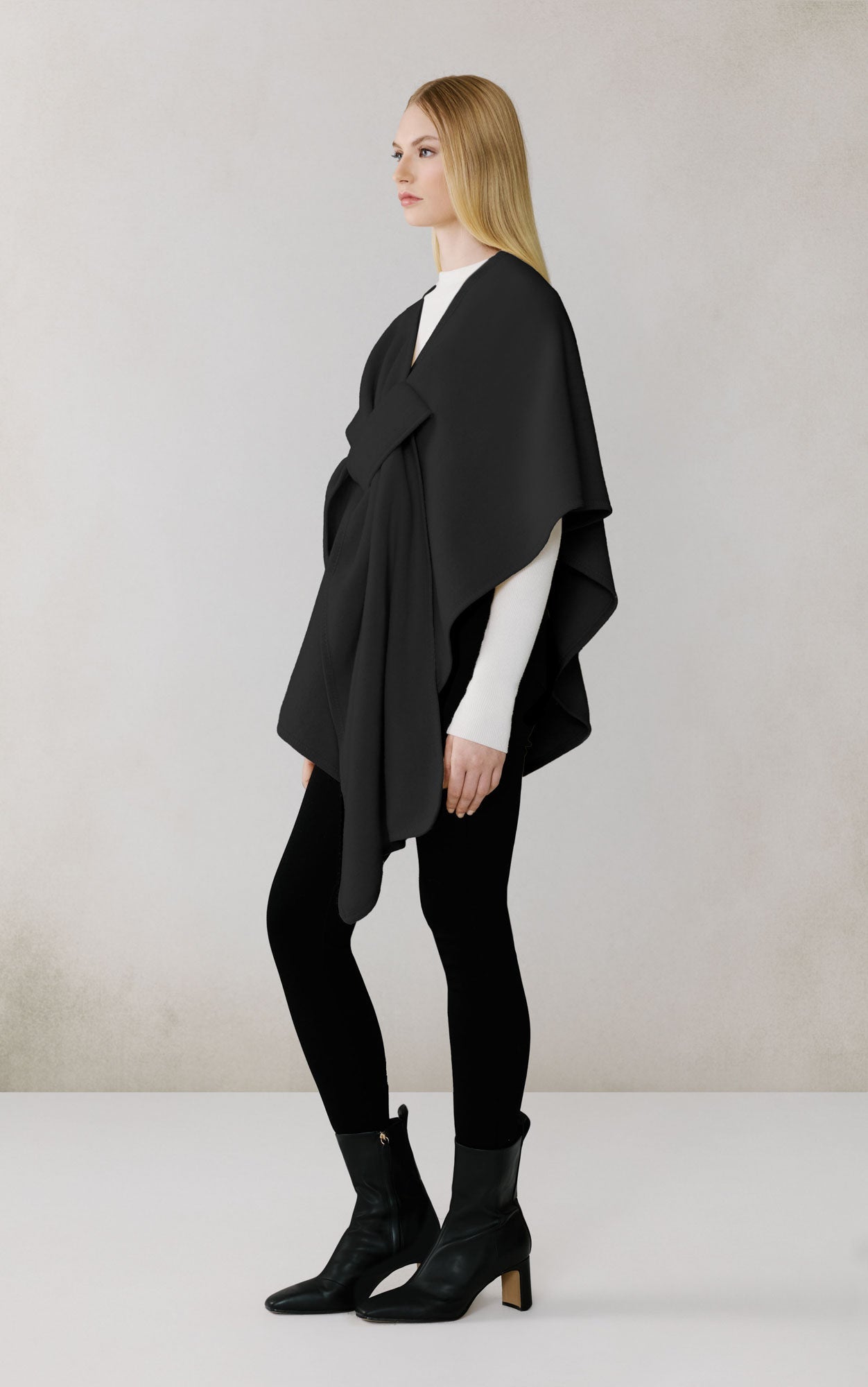 Woman wearing black draped scarf over white top and black pants in studio setting