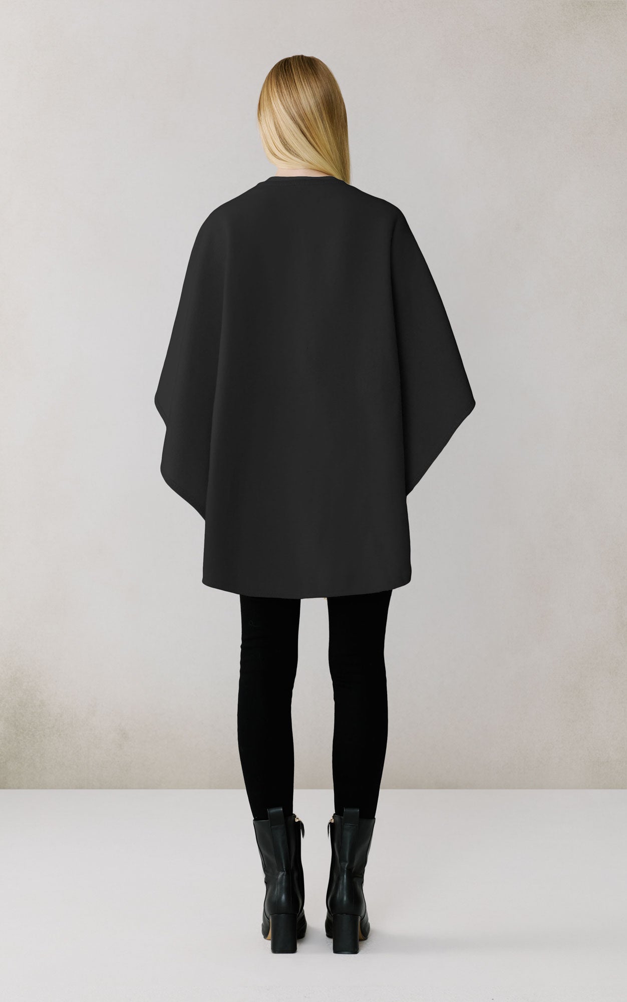 Woman wearing black oversized scarf coat from behind, paired with black leggings and boots