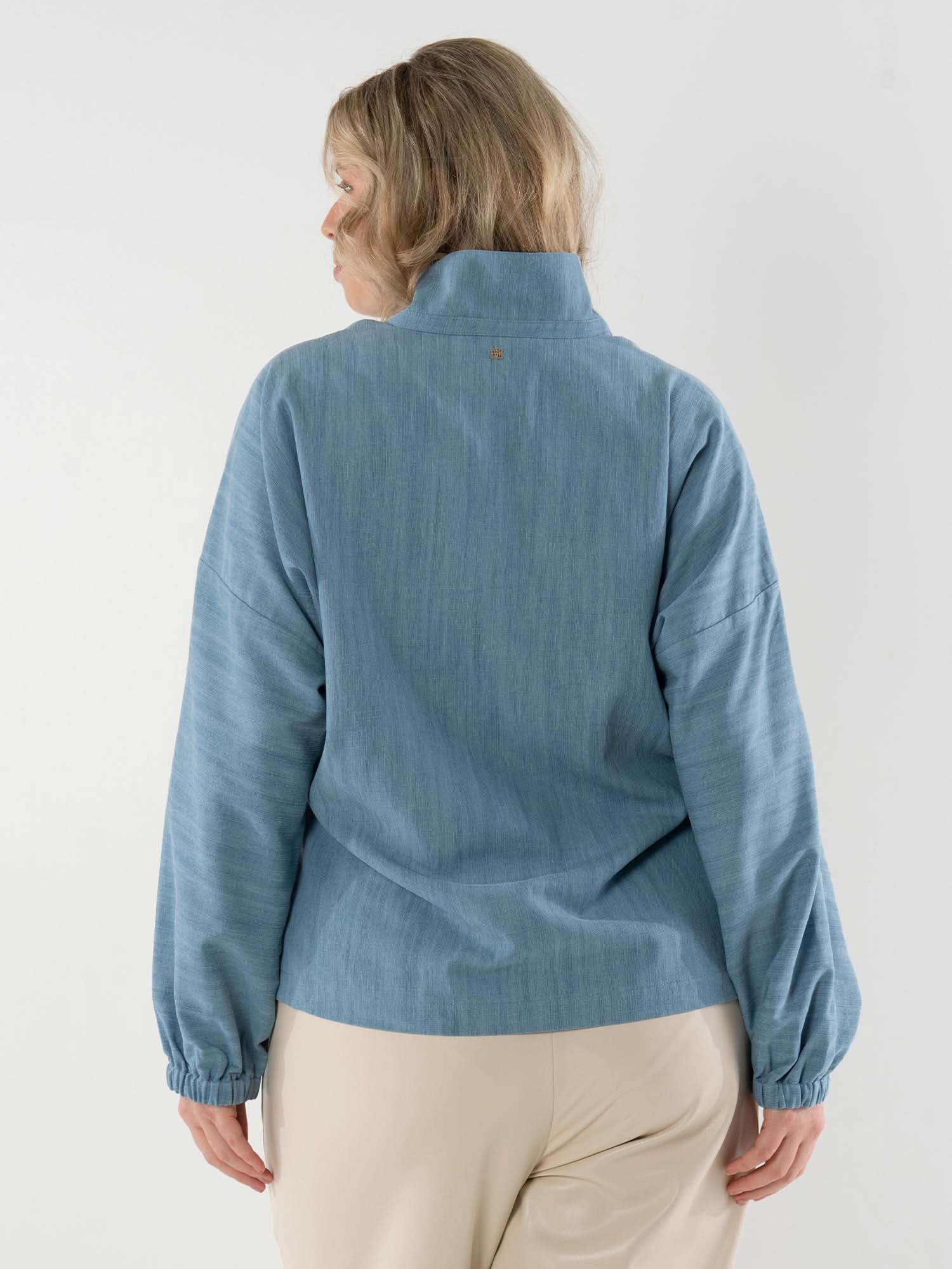 Woman wearing light blue denim pullover with elastic waist, shown from back