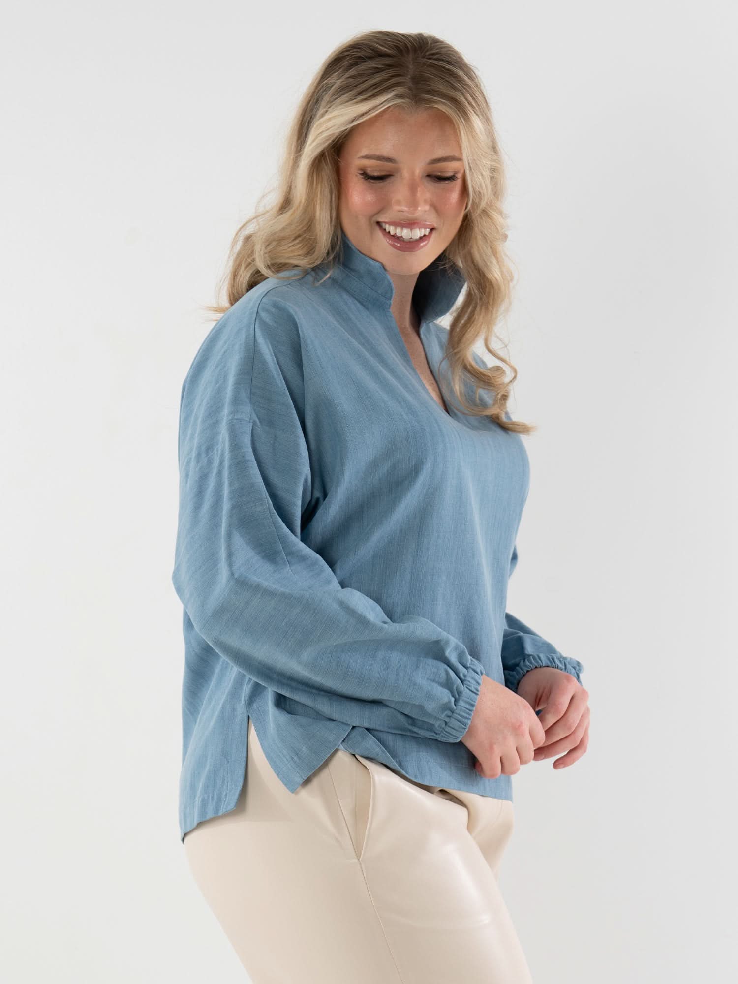 Woman wearing light blue denim long sleeve pullover with elastic cuffs and cream pants