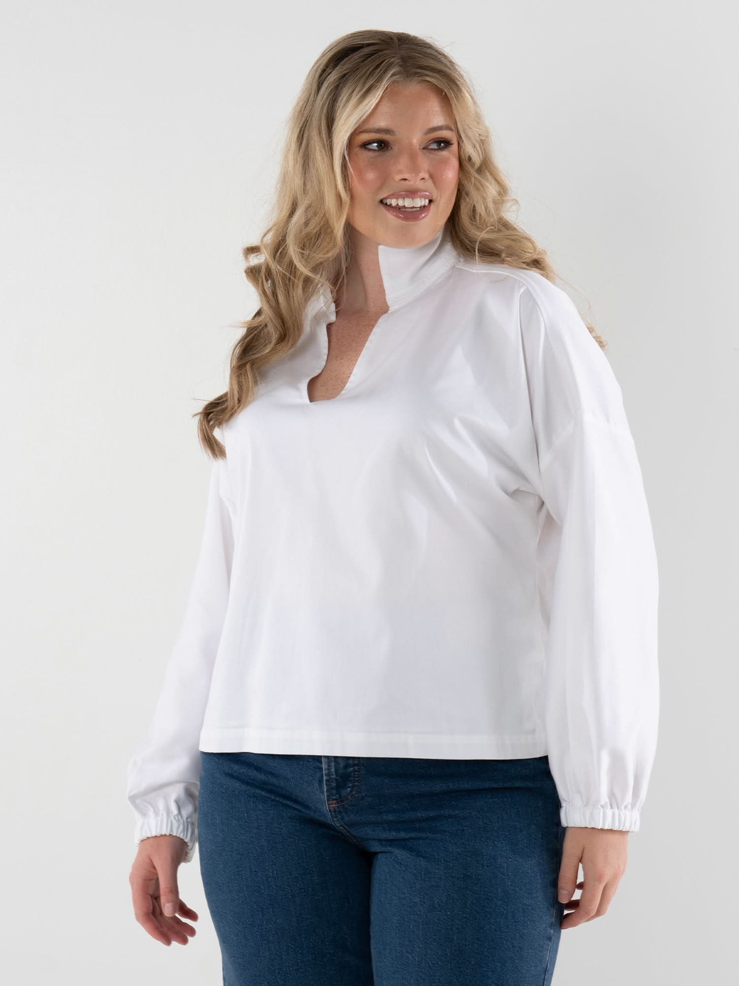Woman wearing white long sleeve pullover top with jeans against neutral background
