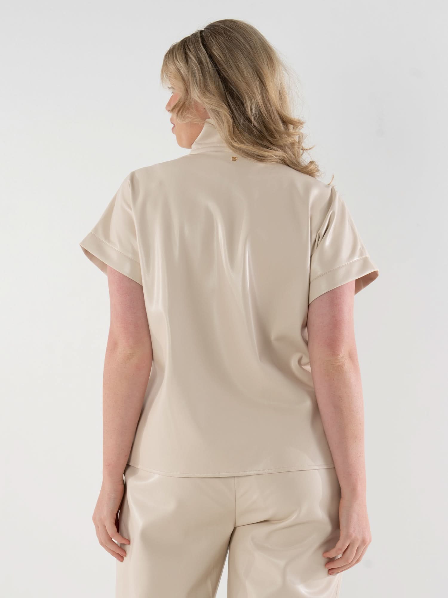 Back view of woman wearing cream vegan leather short-sleeve top with matching pants