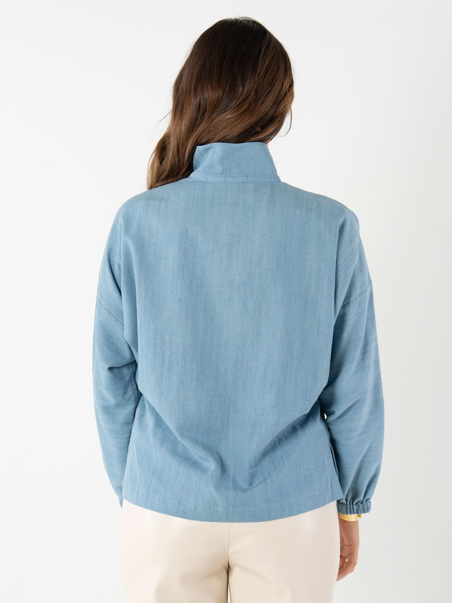 Back view of woman wearing light blue denim long sleeve pullover top
