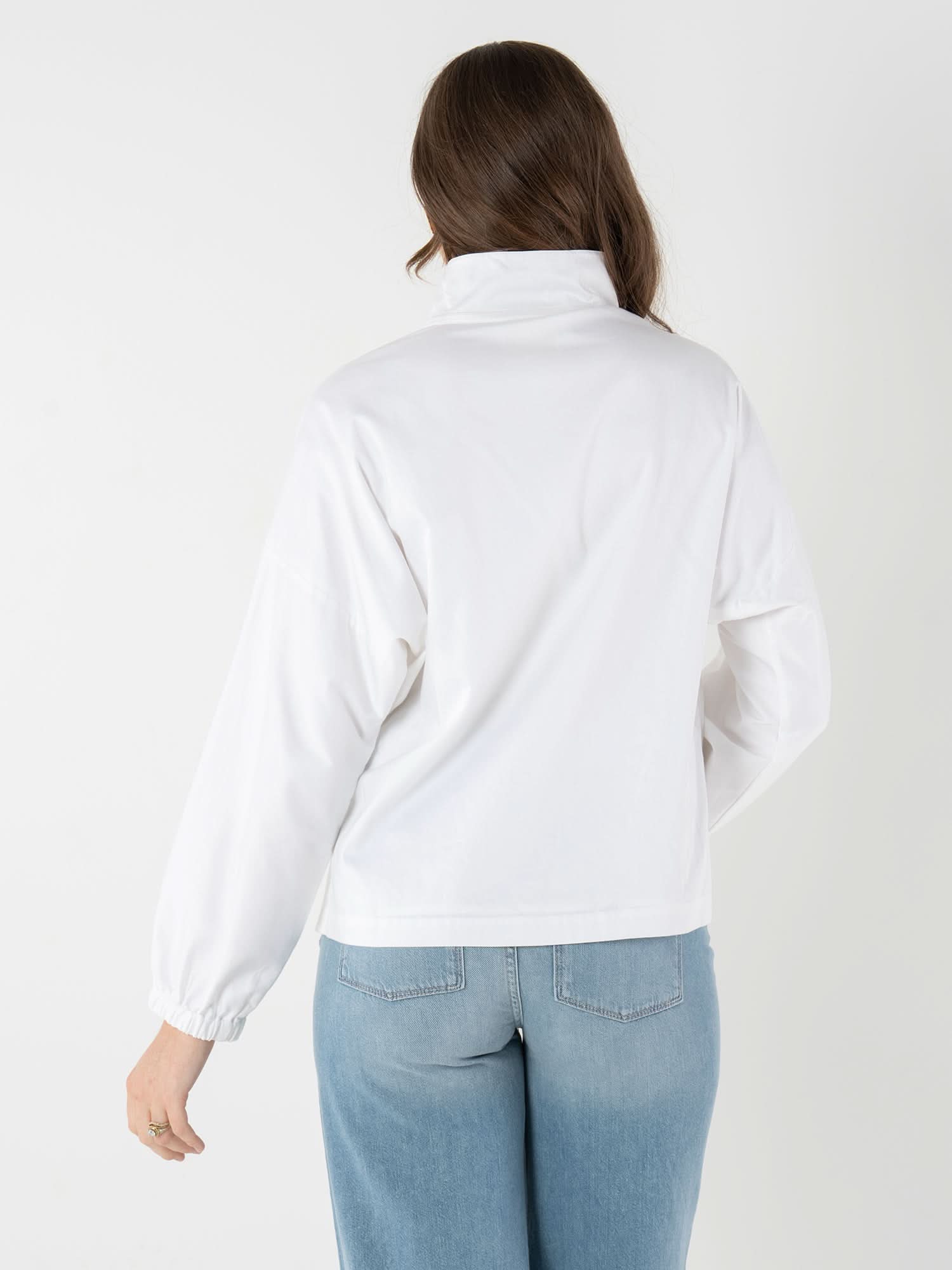 Back view of woman wearing white poplin long sleeve pullover with blue jeans