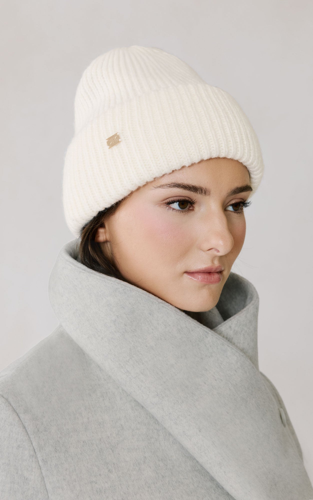 Woman wearing cream colored Soia & Kyo Jaya knit beanie hat with matching coat