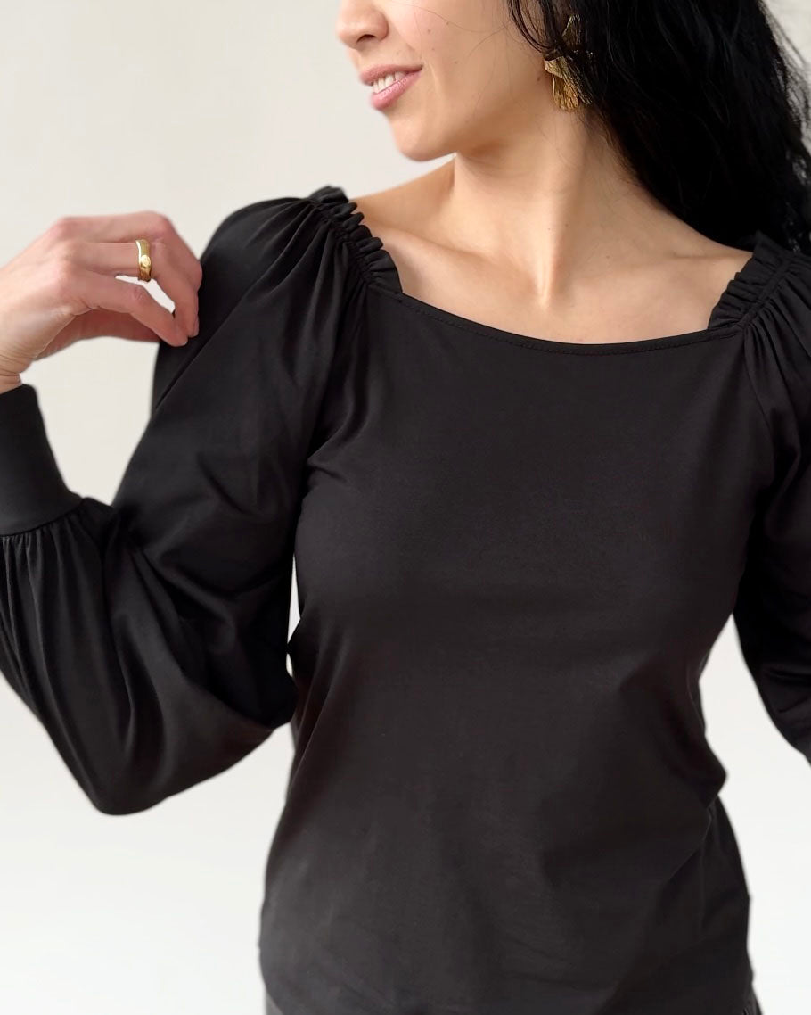 Woman wearing black long-sleeve top with gathered shoulders and balloon sleeves