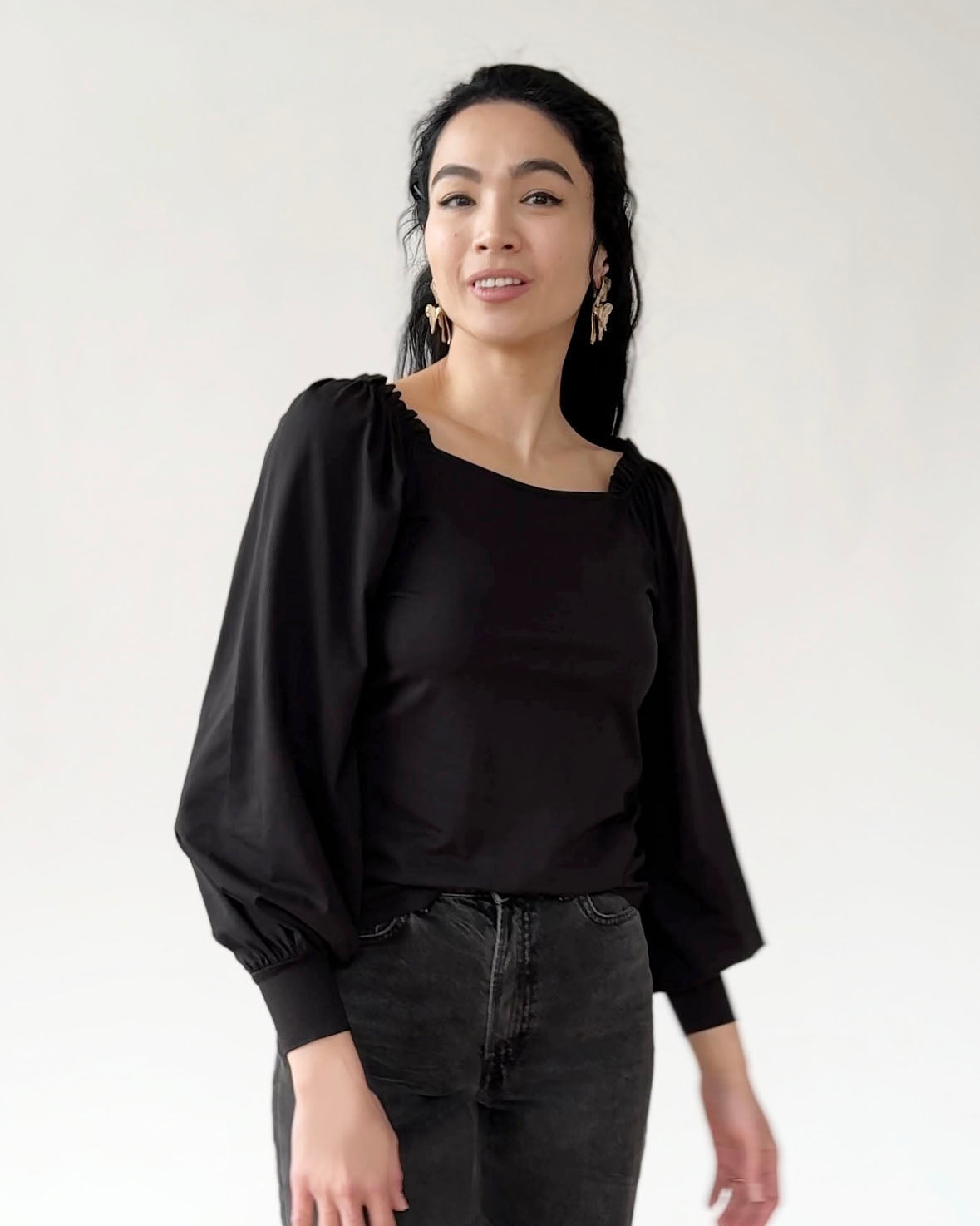 Woman wearing black long-sleeve top with balloon sleeves and ribbed cuffs, styled with dark jeans