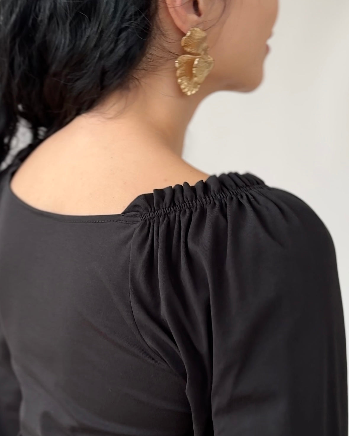 Black off-shoulder top with gathered elastic neckline worn with gold statement earrings