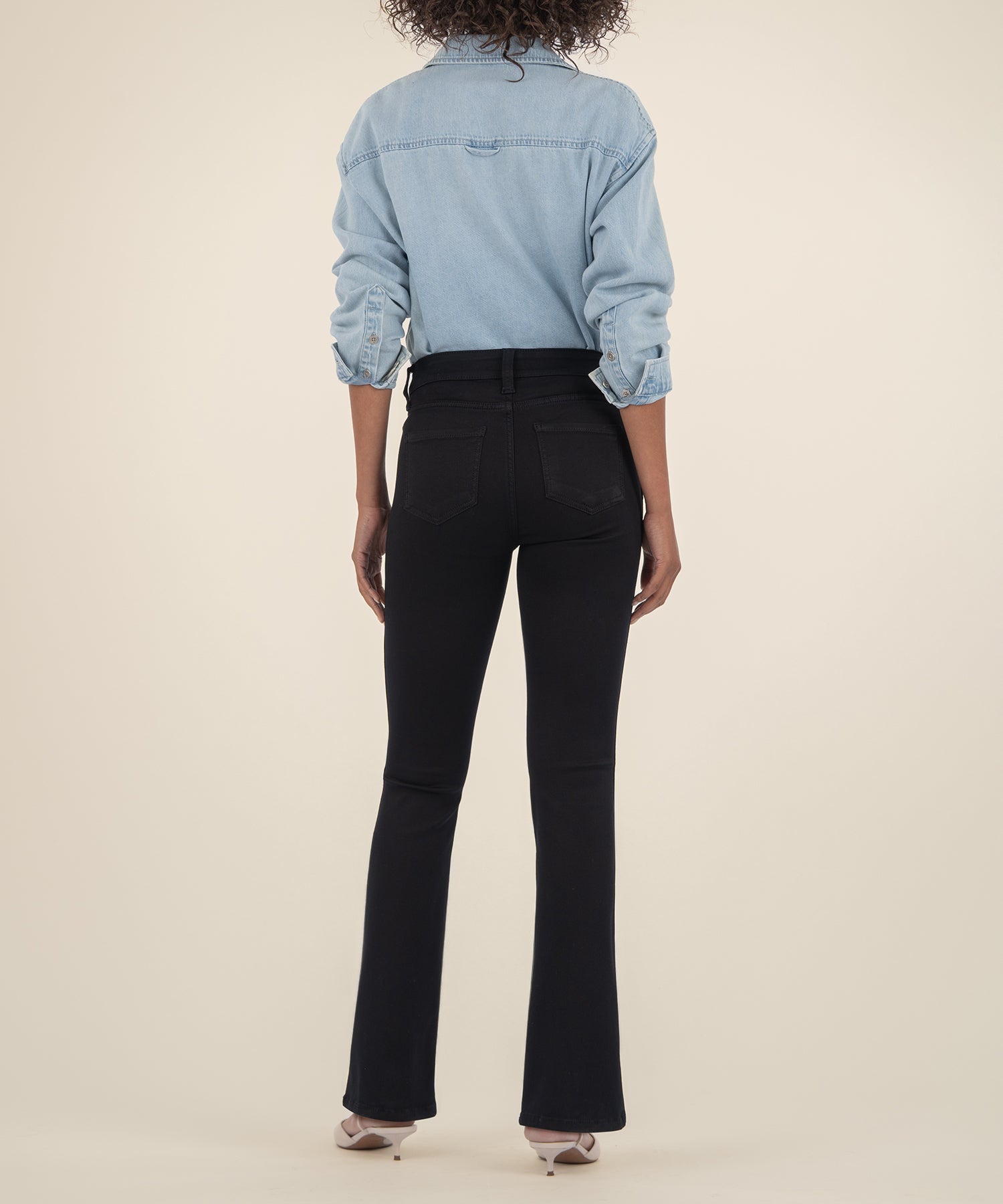 Back view of woman wearing black high-rise bootcut jeans with light denim shirt