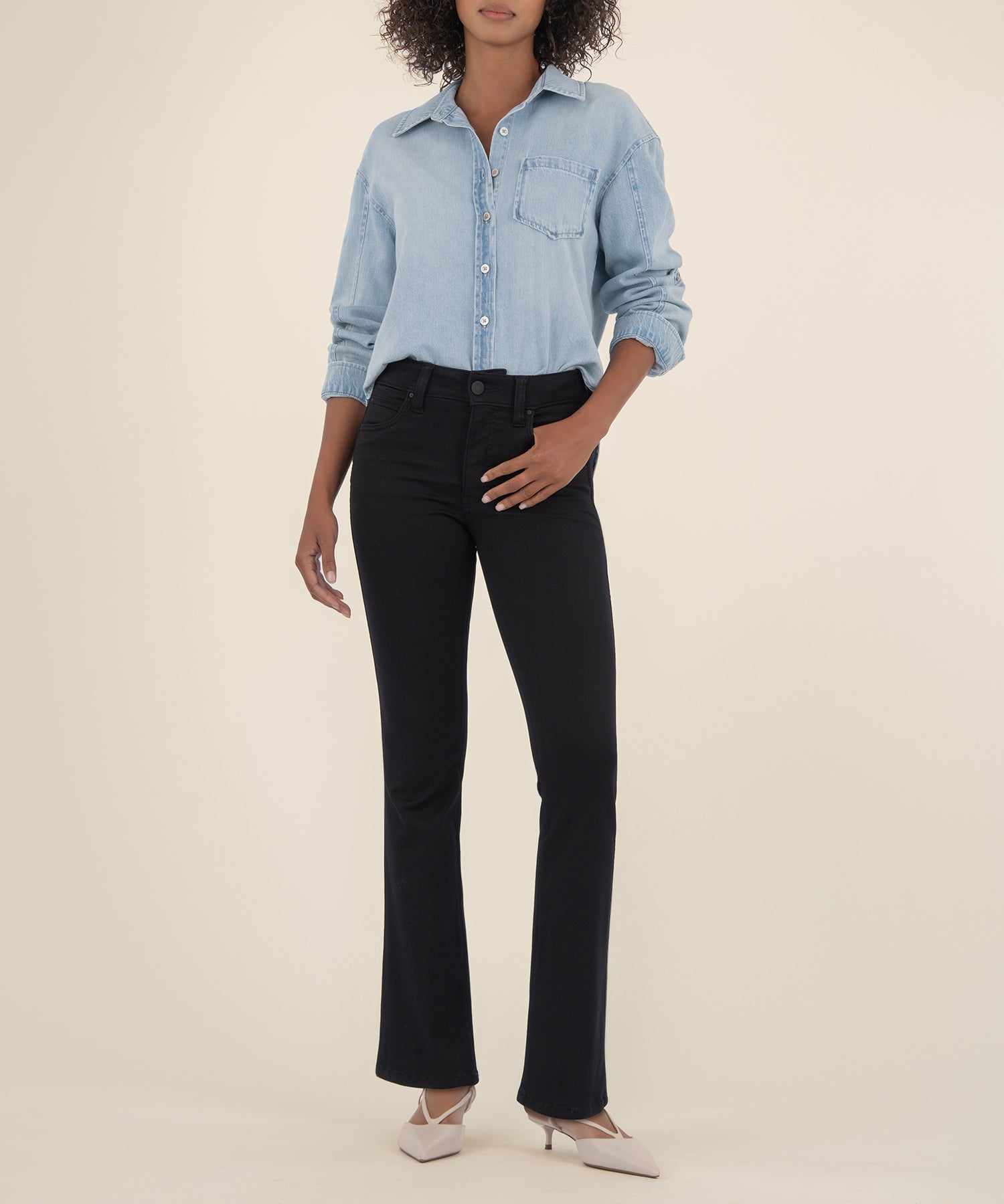 Woman wearing black bootcut jeans with light blue denim shirt on neutral background