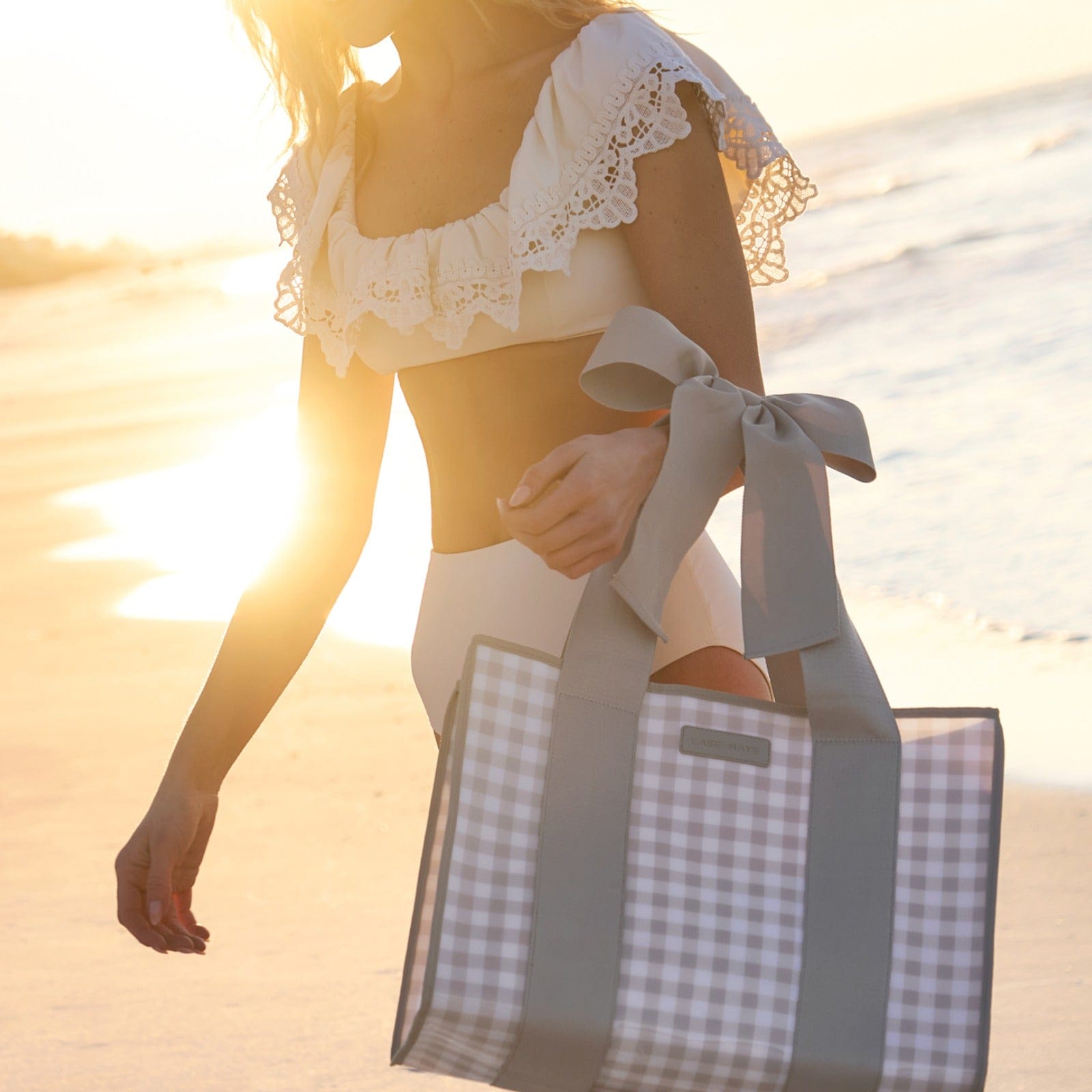 Case-Mate Jelly Bow Tote in Latte Gingham carried by woman walking on beach at sunset