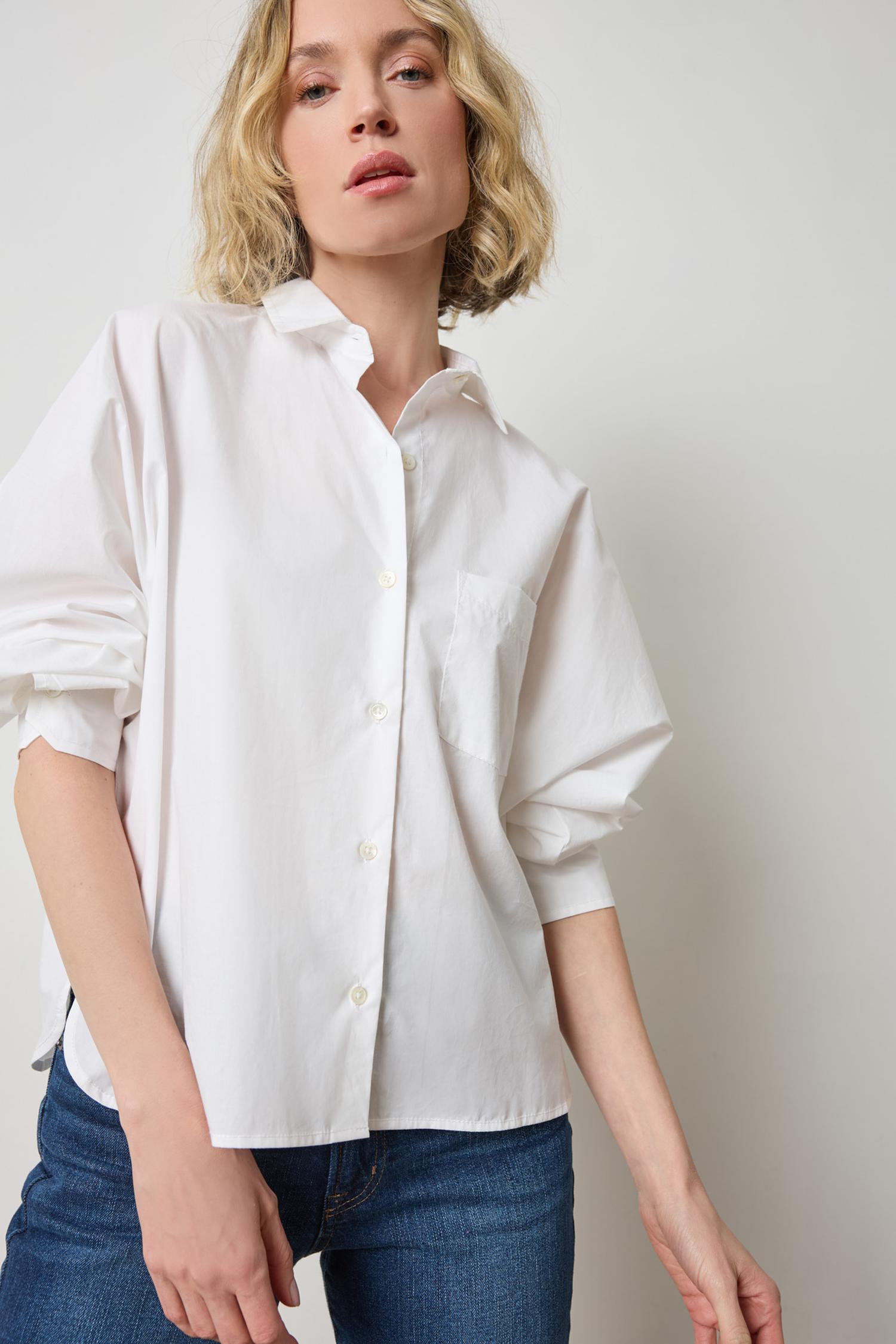 Woman wearing white dolman sleeve button-down blouse with jeans in studio setting