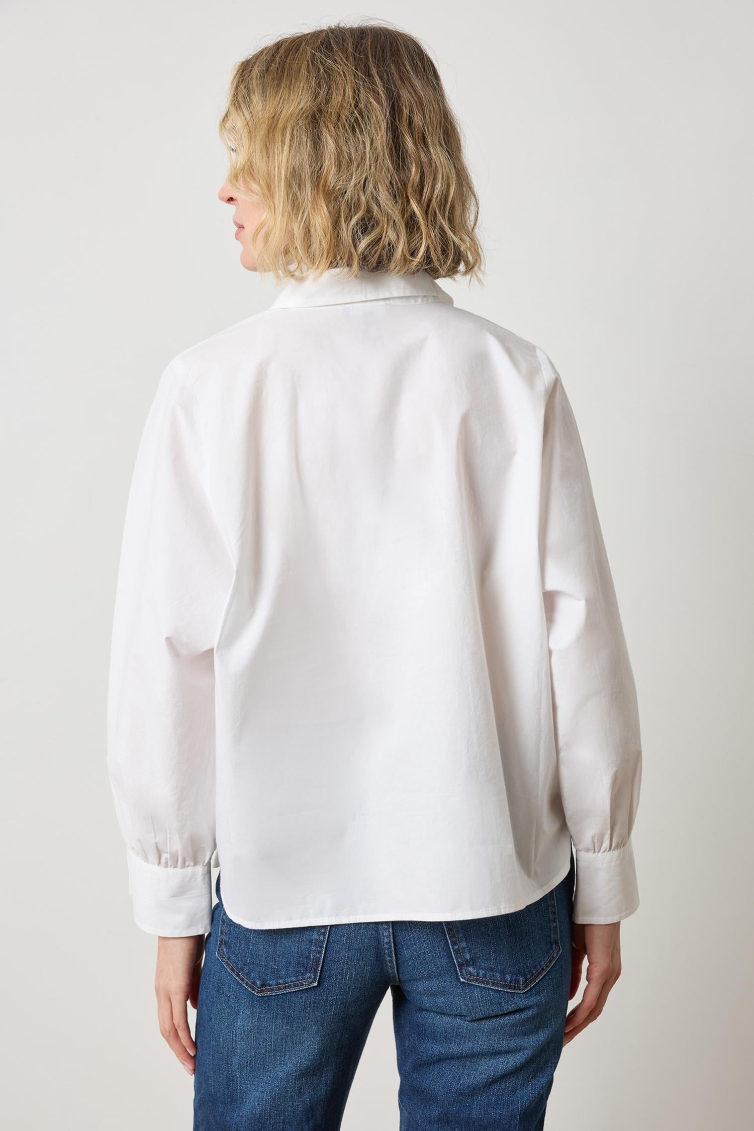 Back view of woman wearing white dolman sleeve button down blouse with jeans