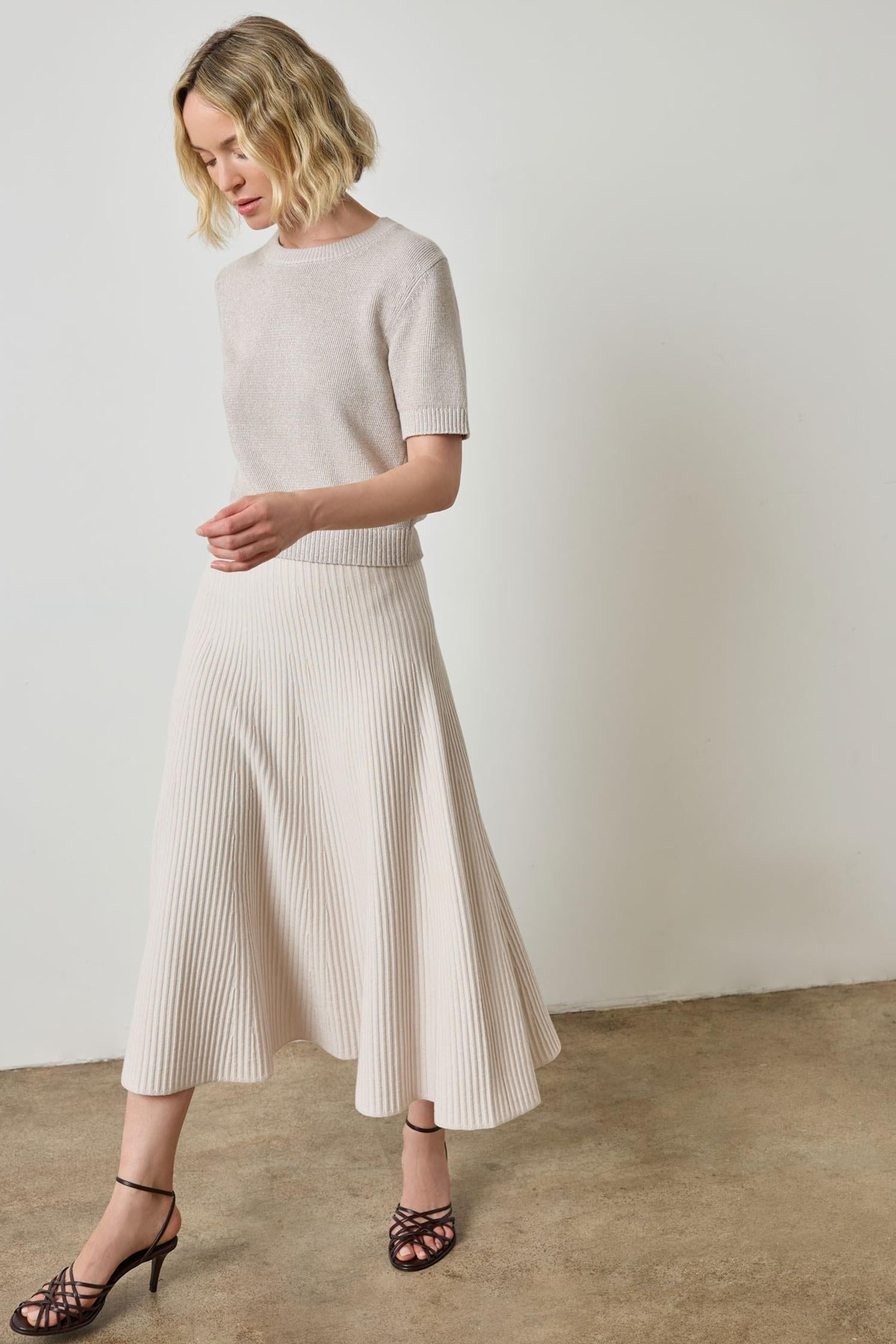 Woman wearing light beige knit short sleeve top and matching flared midi skirt