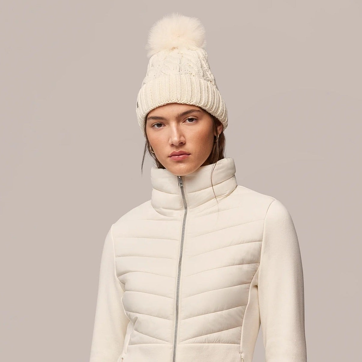Woman wearing cream cable-knit beanie with pom-pom and matching quilted jacket