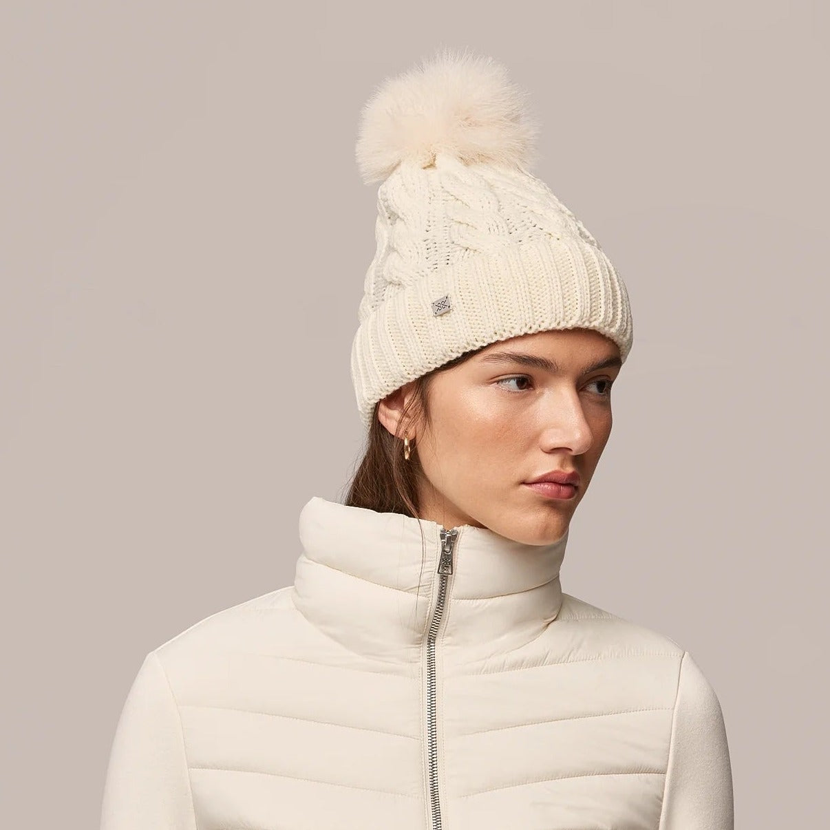 Woman wearing cream cable-knit beanie with pom-pom and matching quilted jacket