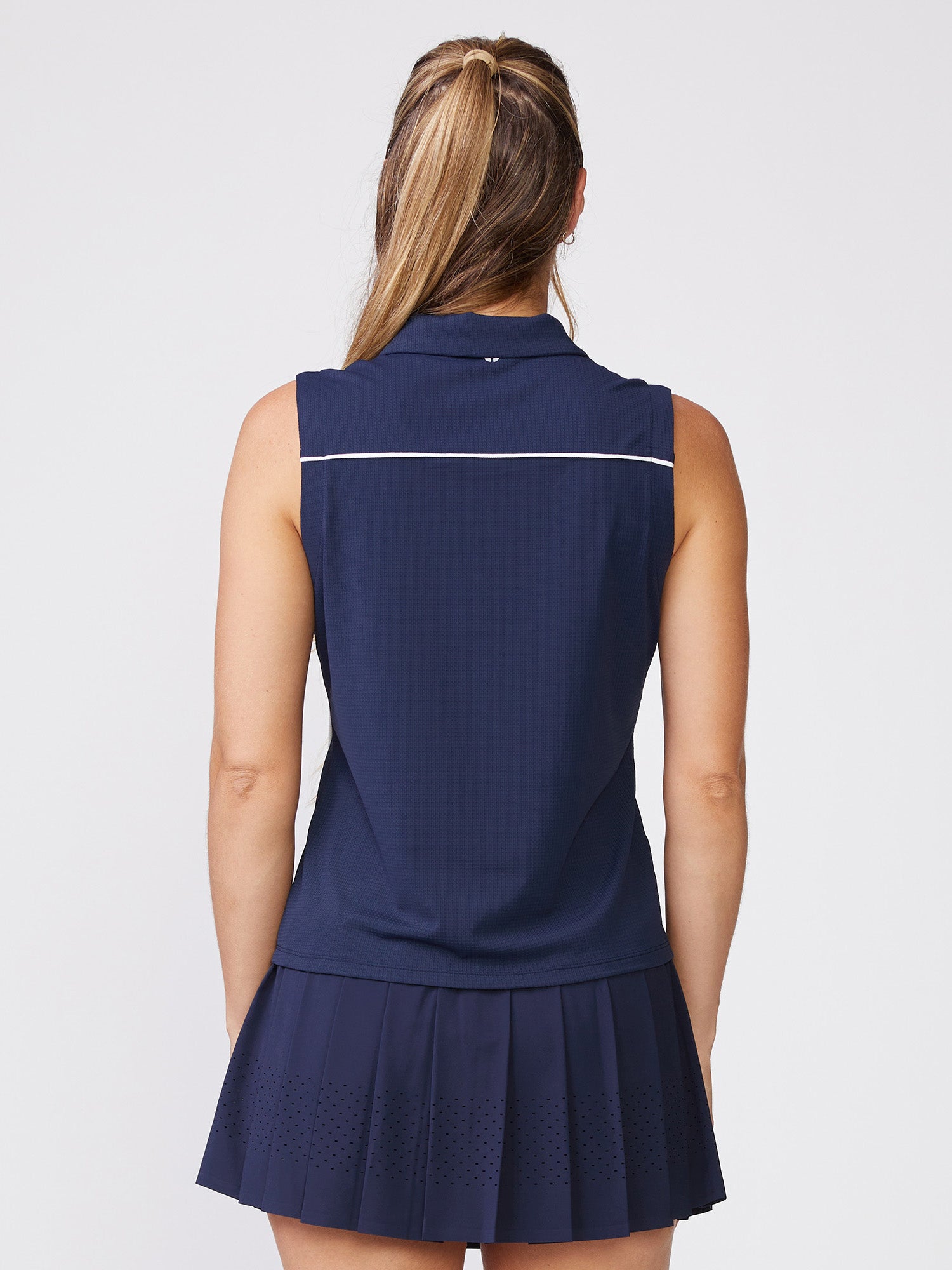 Back view of woman wearing navy sleeveless quarter-zip polo with matching pleated skirt