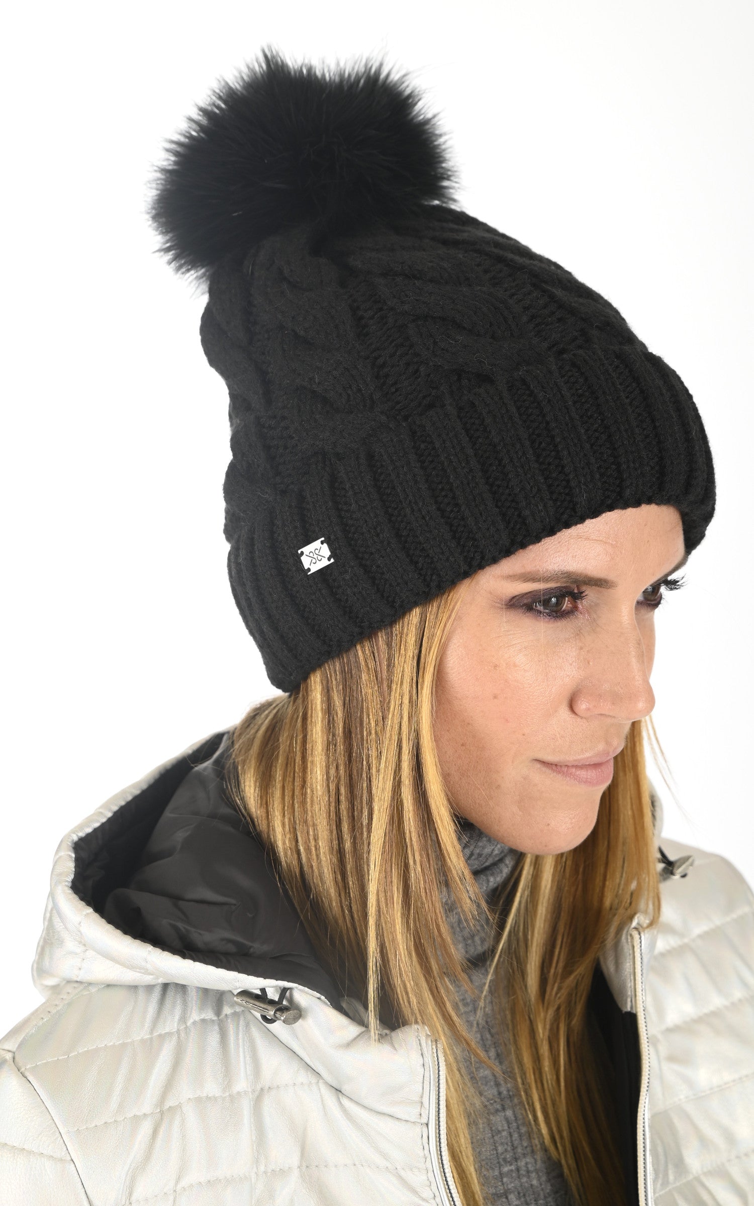 Woman wearing black cable-knit beanie with fur pom-pom and white winter jacket