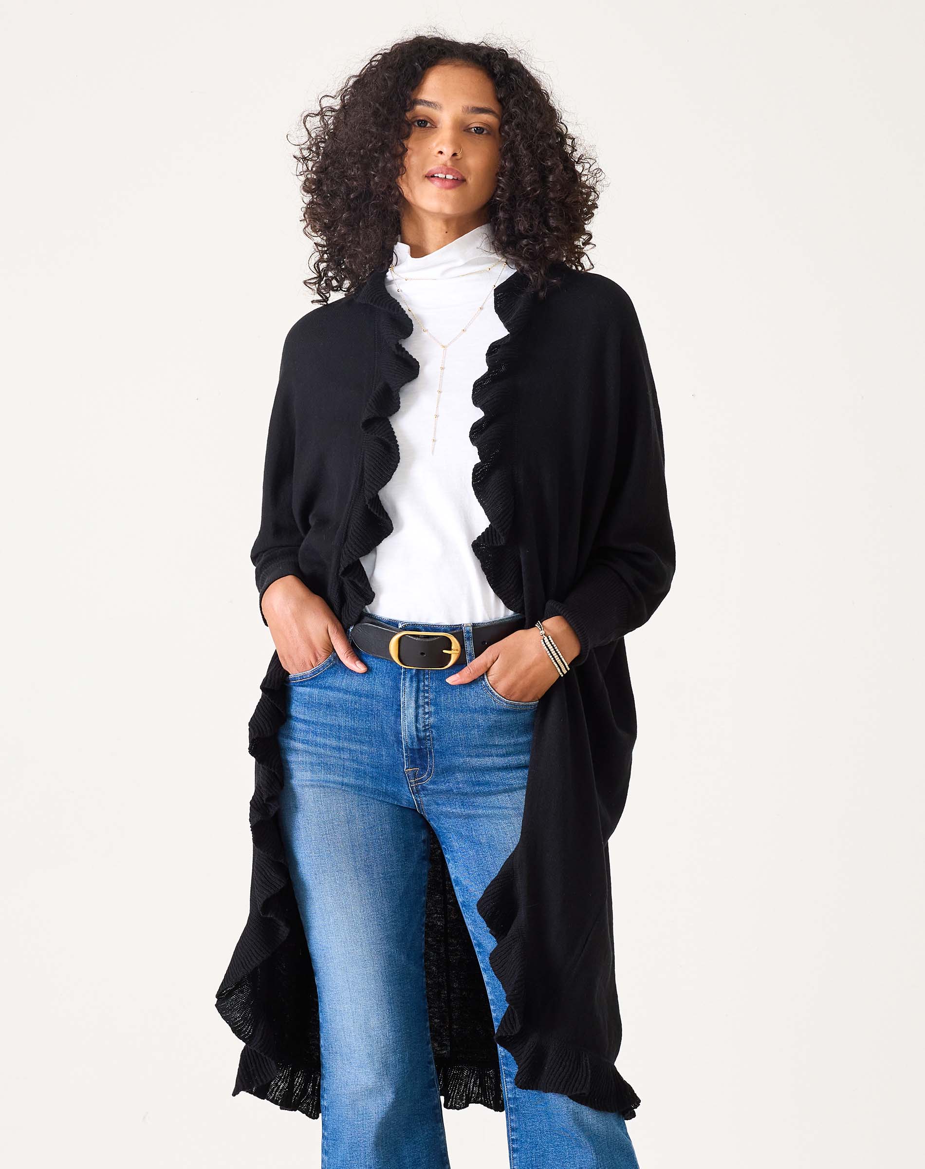 Woman wearing a black long ruffled kimono cardigan over white turtleneck and blue jeans
