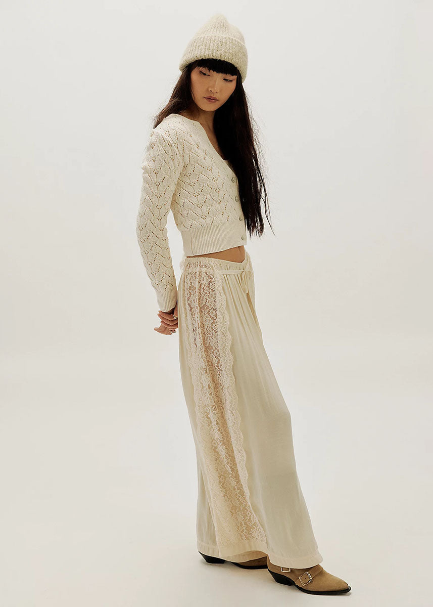 Woman wearing ivory pointelle knit cardigan with matching wide-leg lace pants and knit beanie