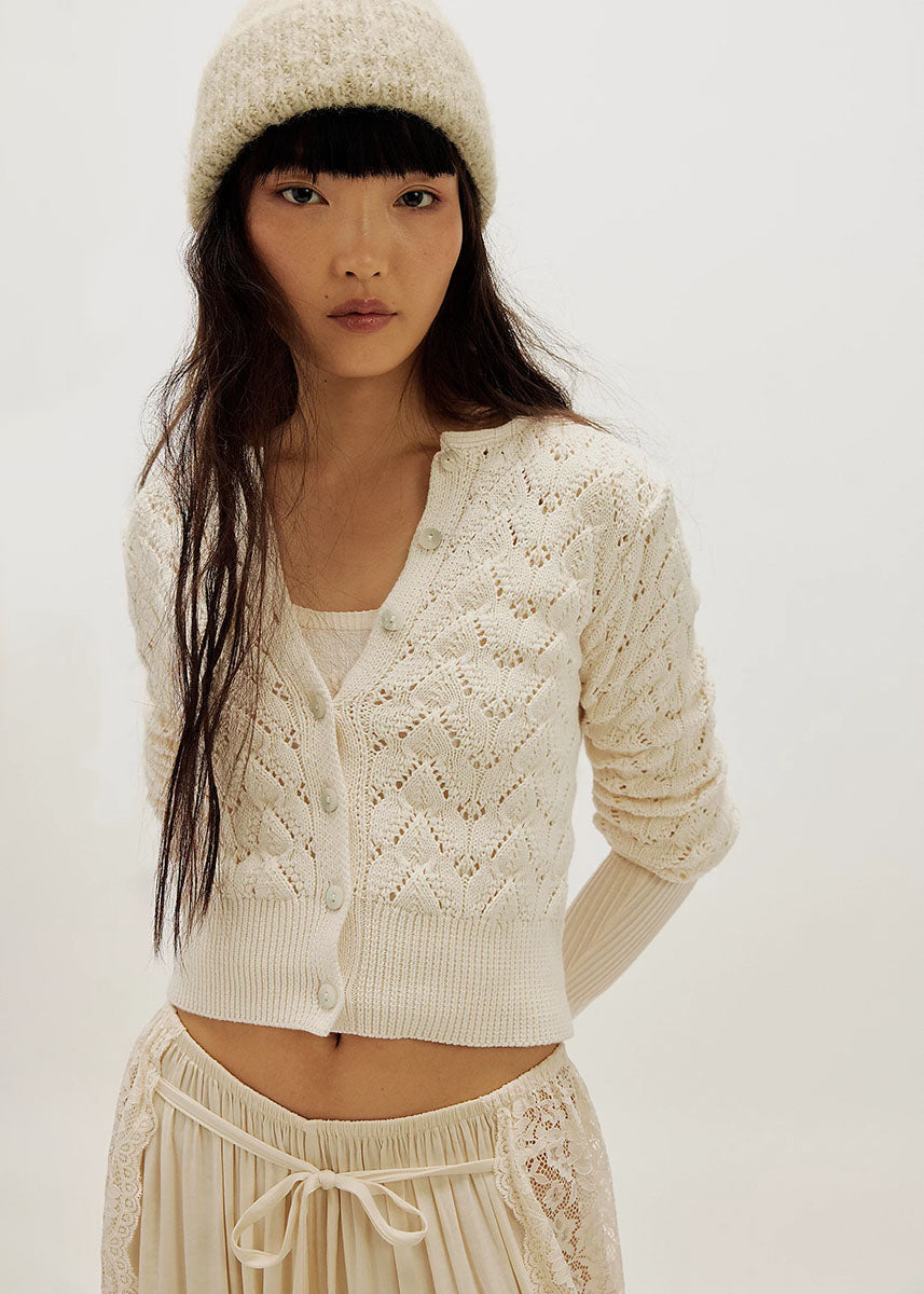 Woman wearing ivory pointelle knit cardigan sweater with matching beanie and skirt