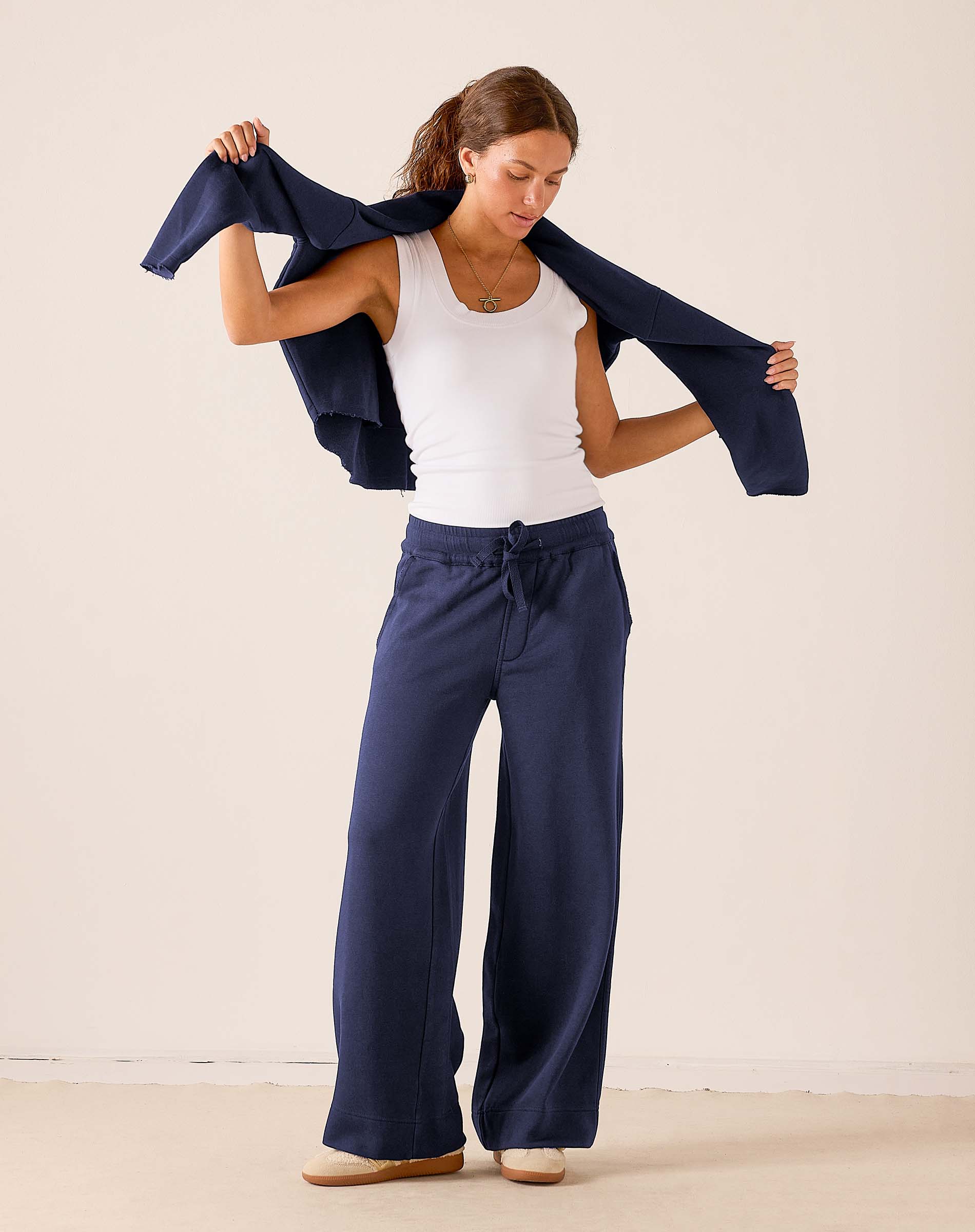 Woman wearing wide-leg navy cadet blue fleece sweatpants with drawstring waist and white tank top