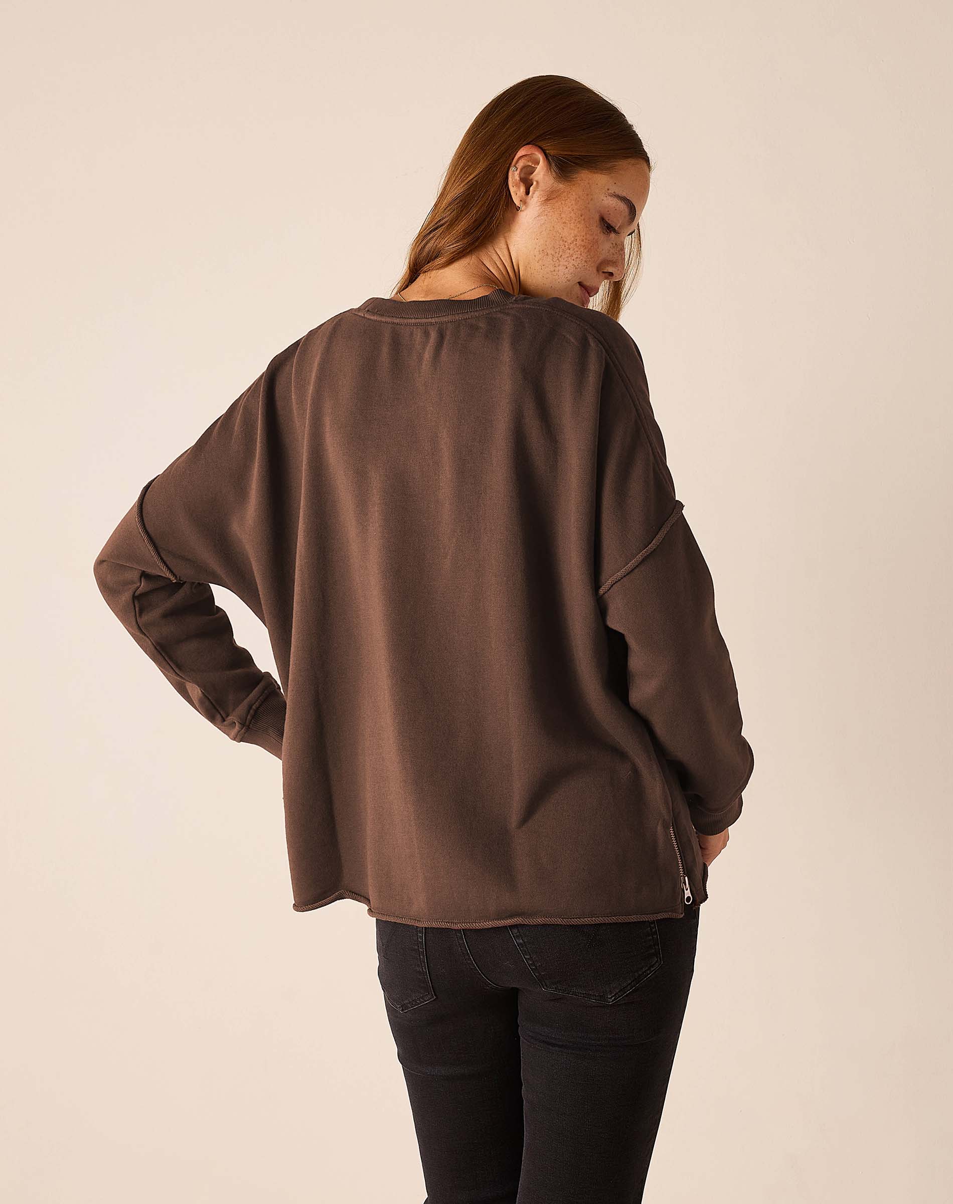 Woman wearing oversized espresso brown crewneck sweatshirt with zip side detail, back view