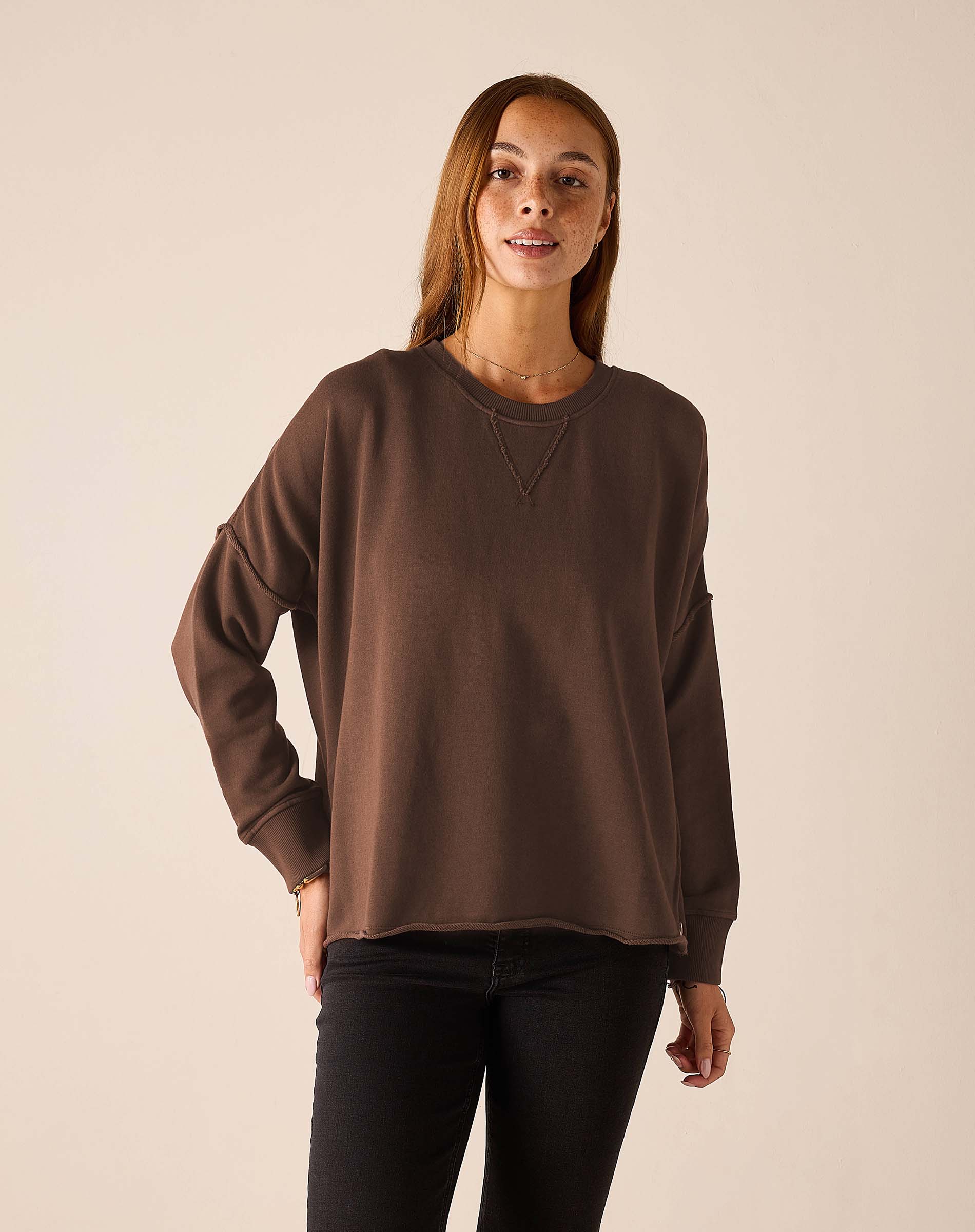 Woman wearing oversized espresso brown crewneck sweatshirt with exposed seam details and black jeans