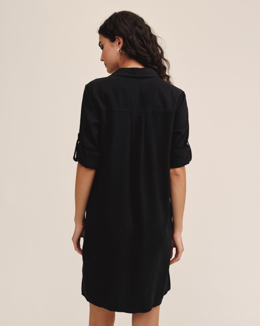 Woman wearing black long sleeve A-line shirt dress with rolled sleeves, back view
